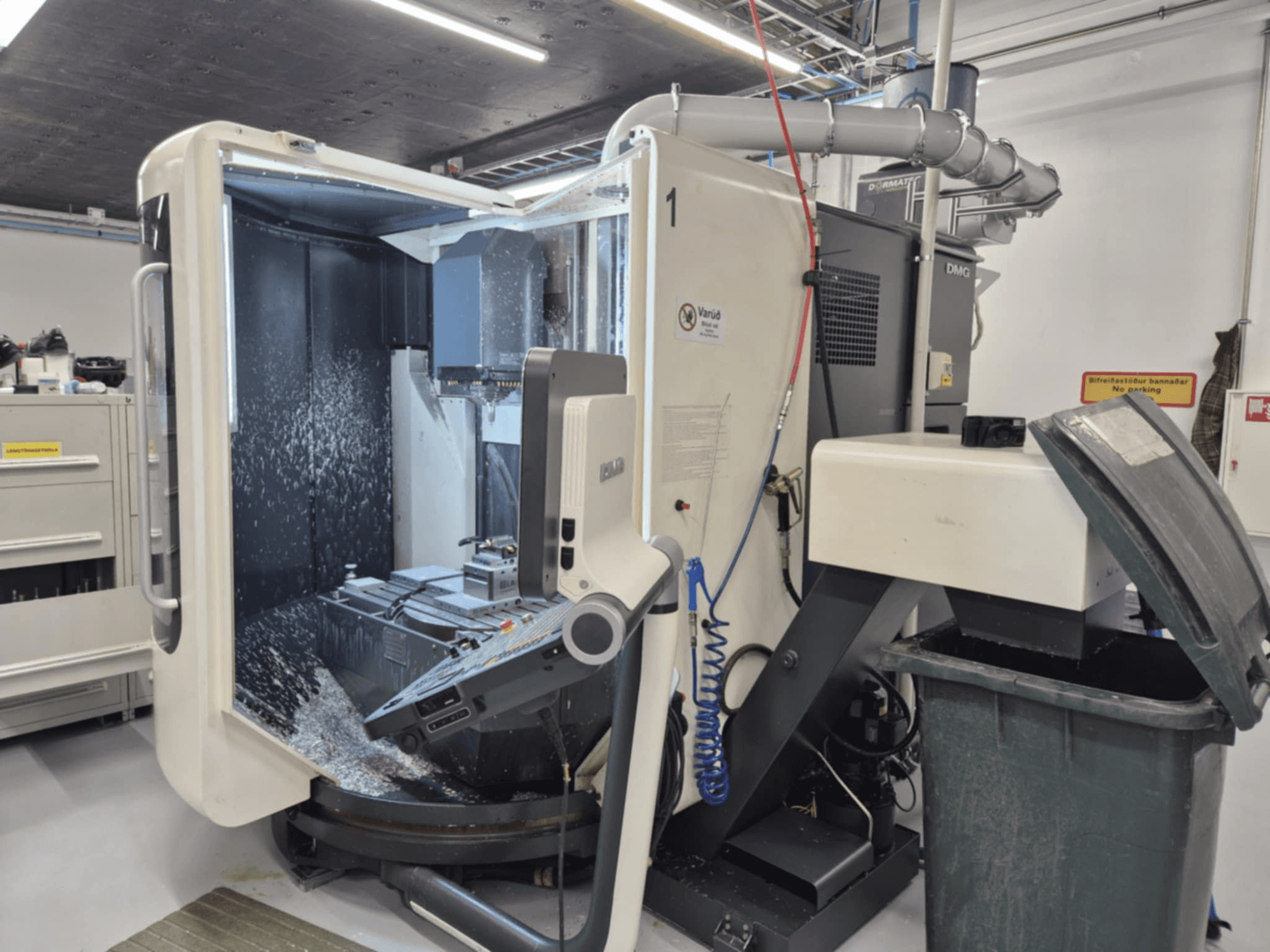 Open DMG milling machine with coolant spray, displaying metal shavings and tool controls, viewed from the front.