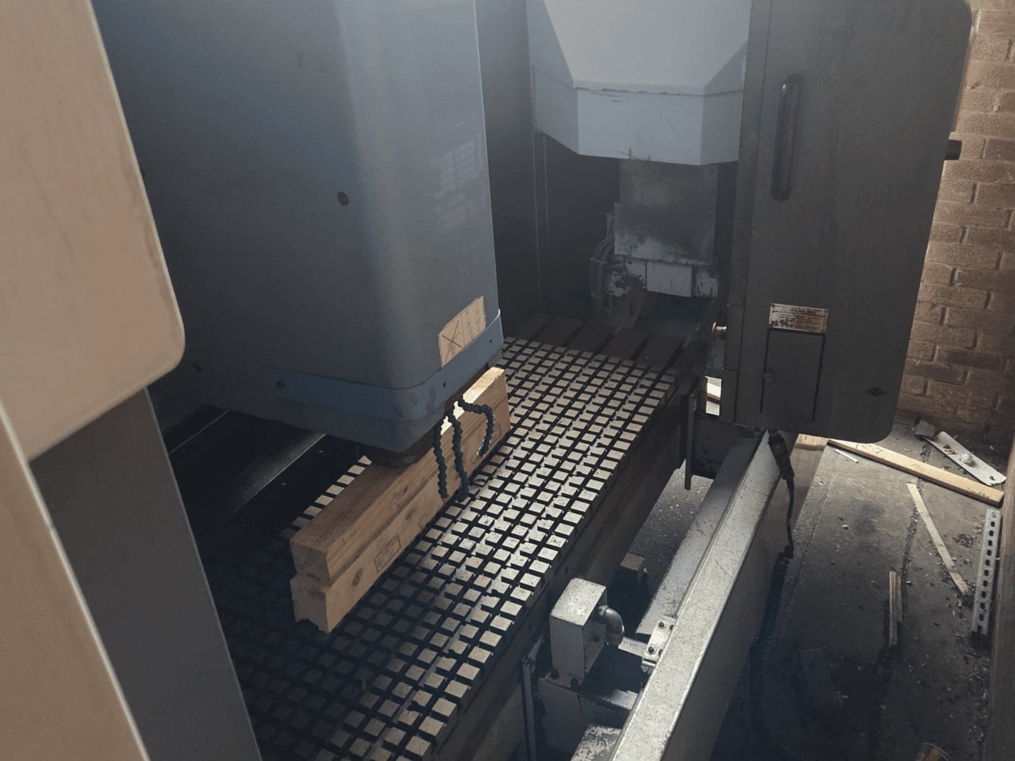 CNC machine front view with wooden planks on a grid table, showcasing tools and controls on the side.