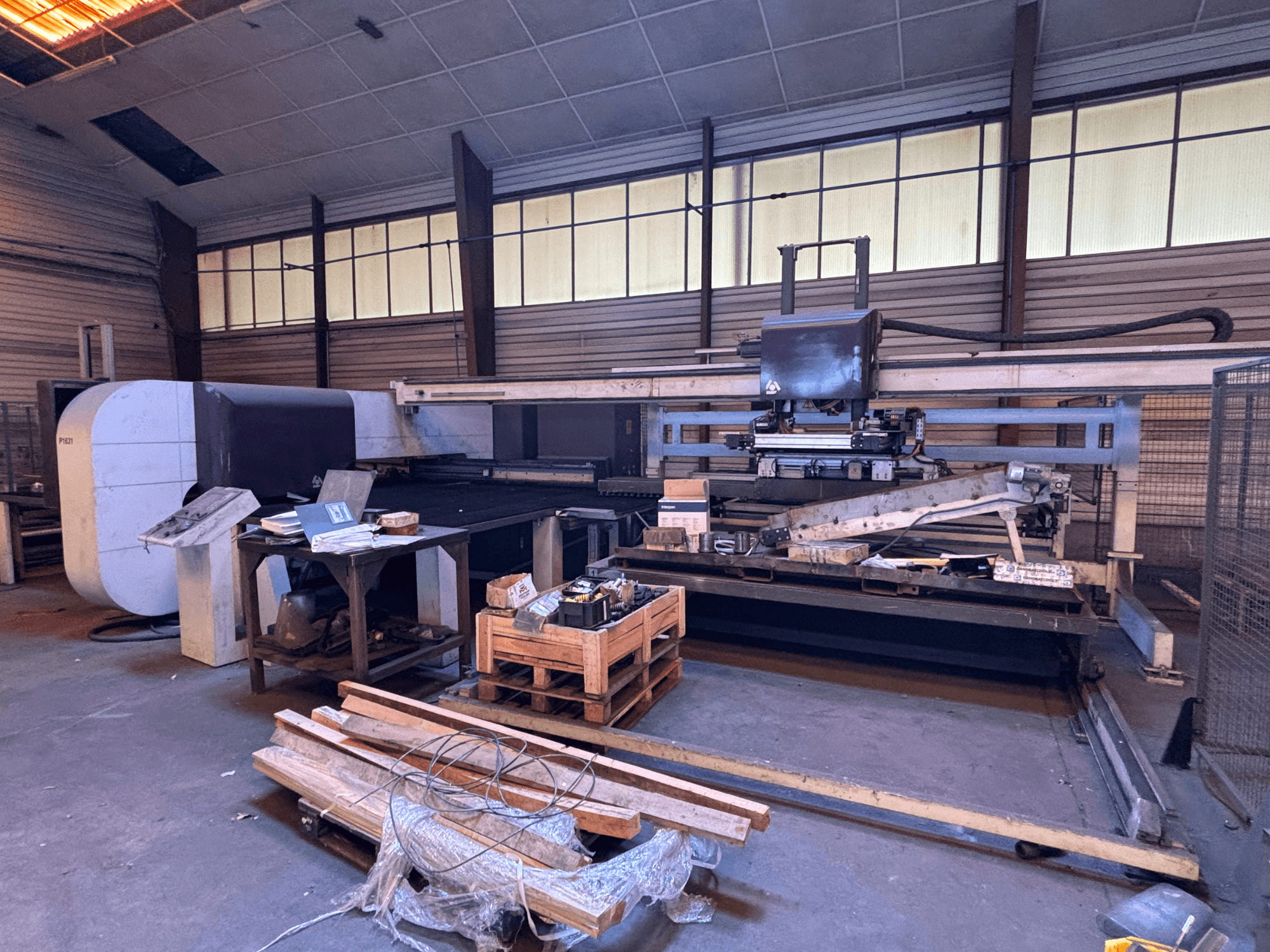 CNC punching machine DANOBAT P1631 in a workshop, front view, surrounded by materials and tools on a cluttered floor.