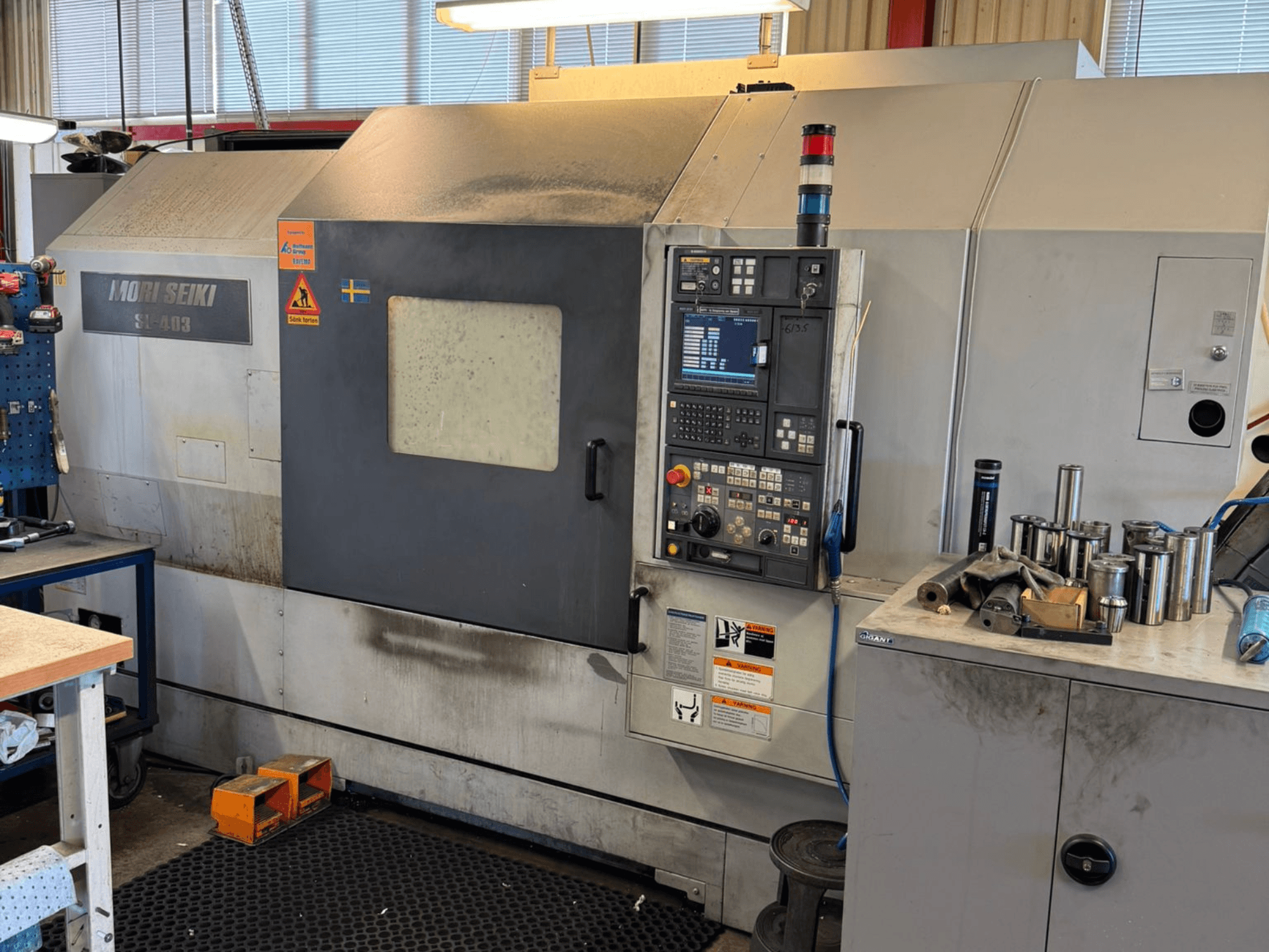 MORI SEIKI SL-403BMC/800 horizontal turning machine in a workshop, showing control panel and nearby tools, side view.
