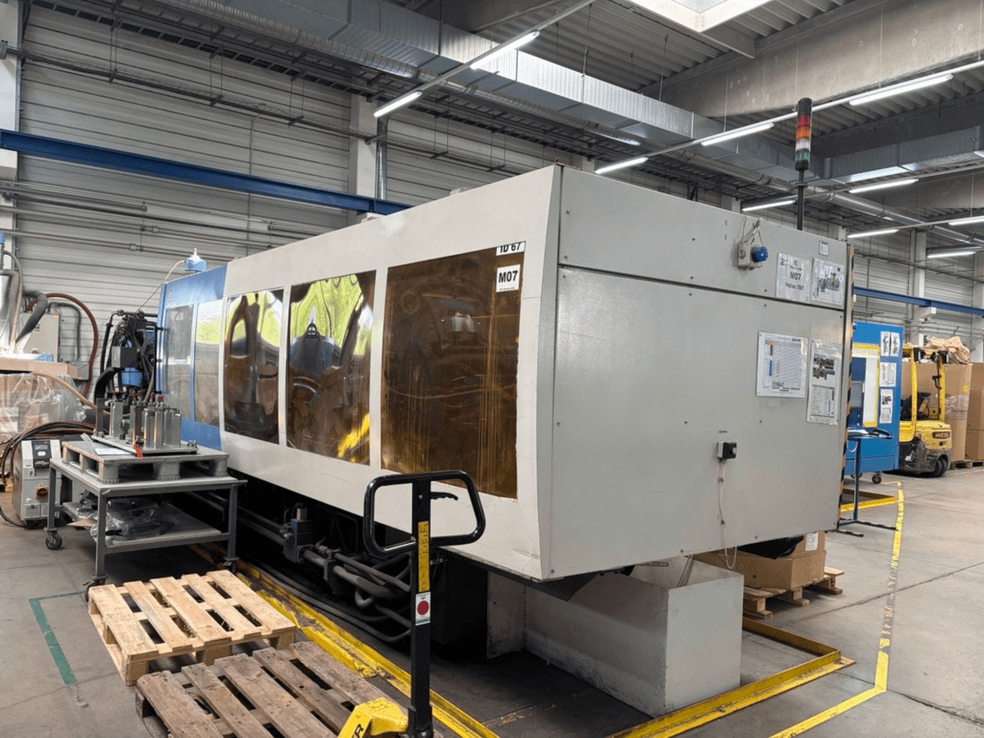 HAITIAN 7000/5000 hydraulic injection moulding machine in a factory, side view with control panels and safety lights visible.