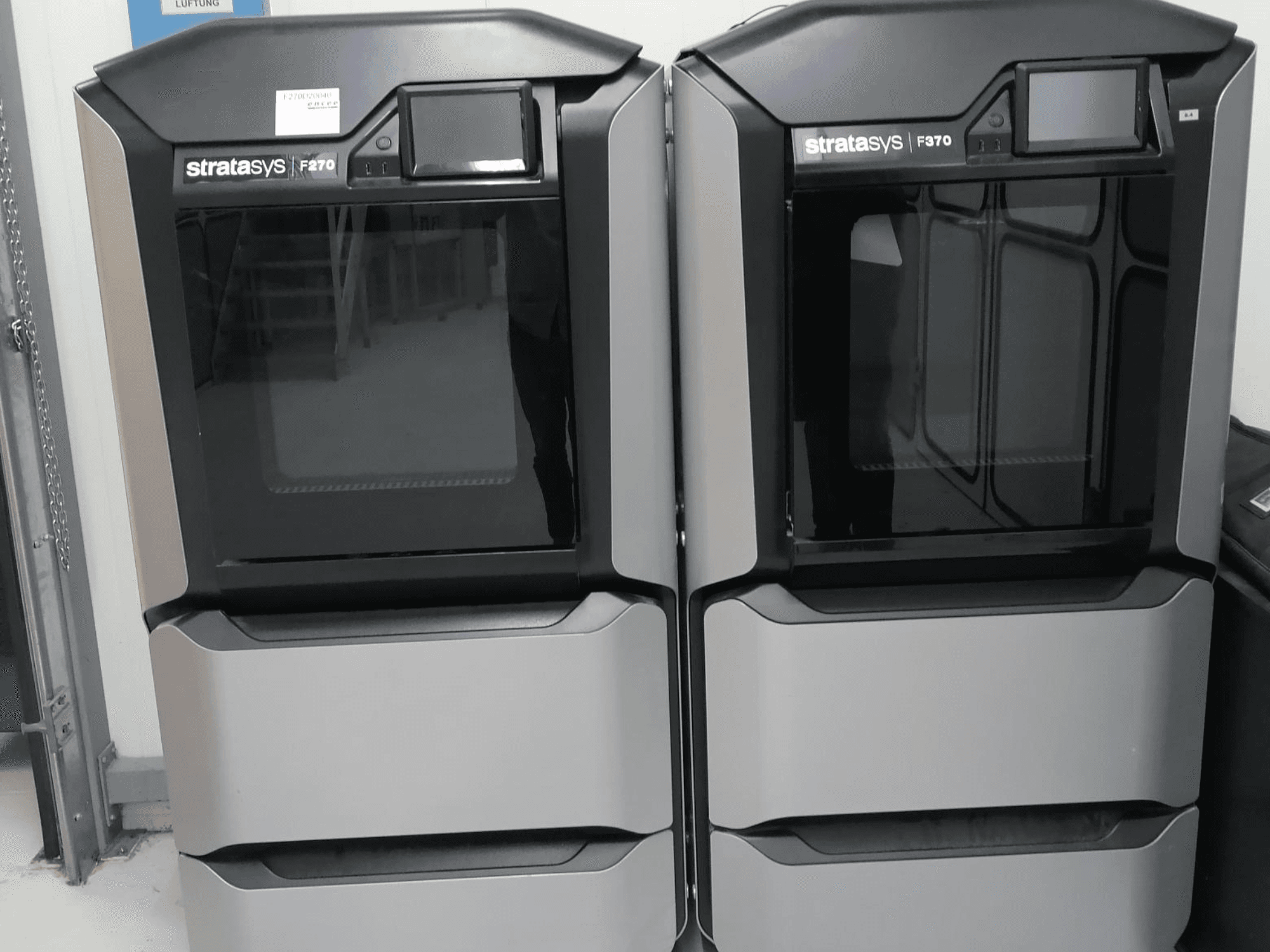 Stratasys F270 plastic 3D printer front view, featuring dual machines with sleek gray exteriors and digital displays.