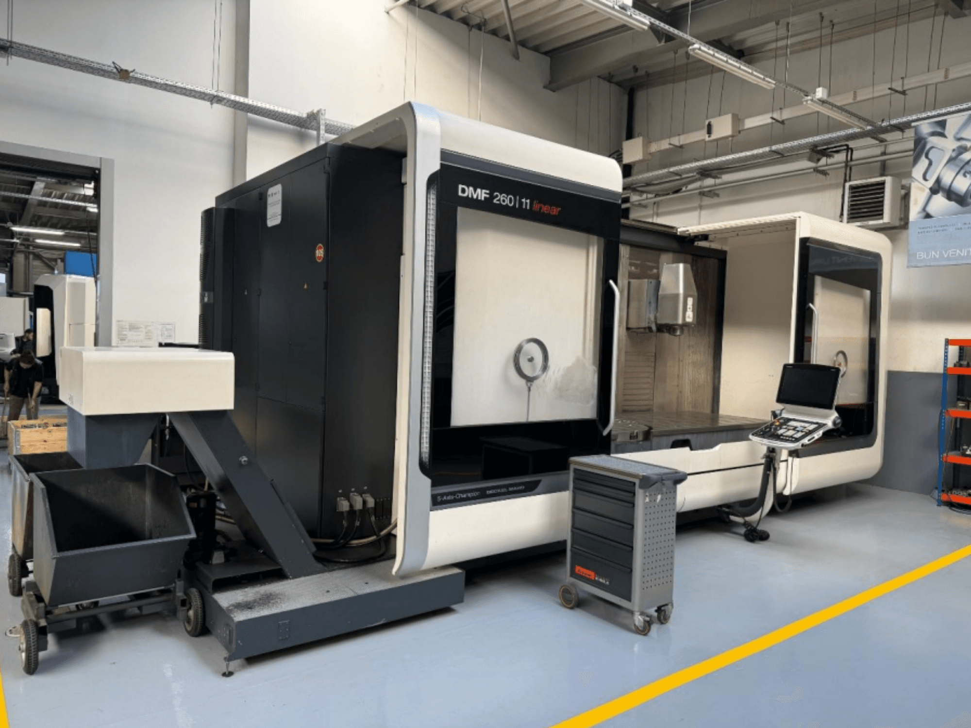DMG MORI DMF 260 Linear milling machine shown from the front, with a tool control panel and a mobile tool cart nearby.