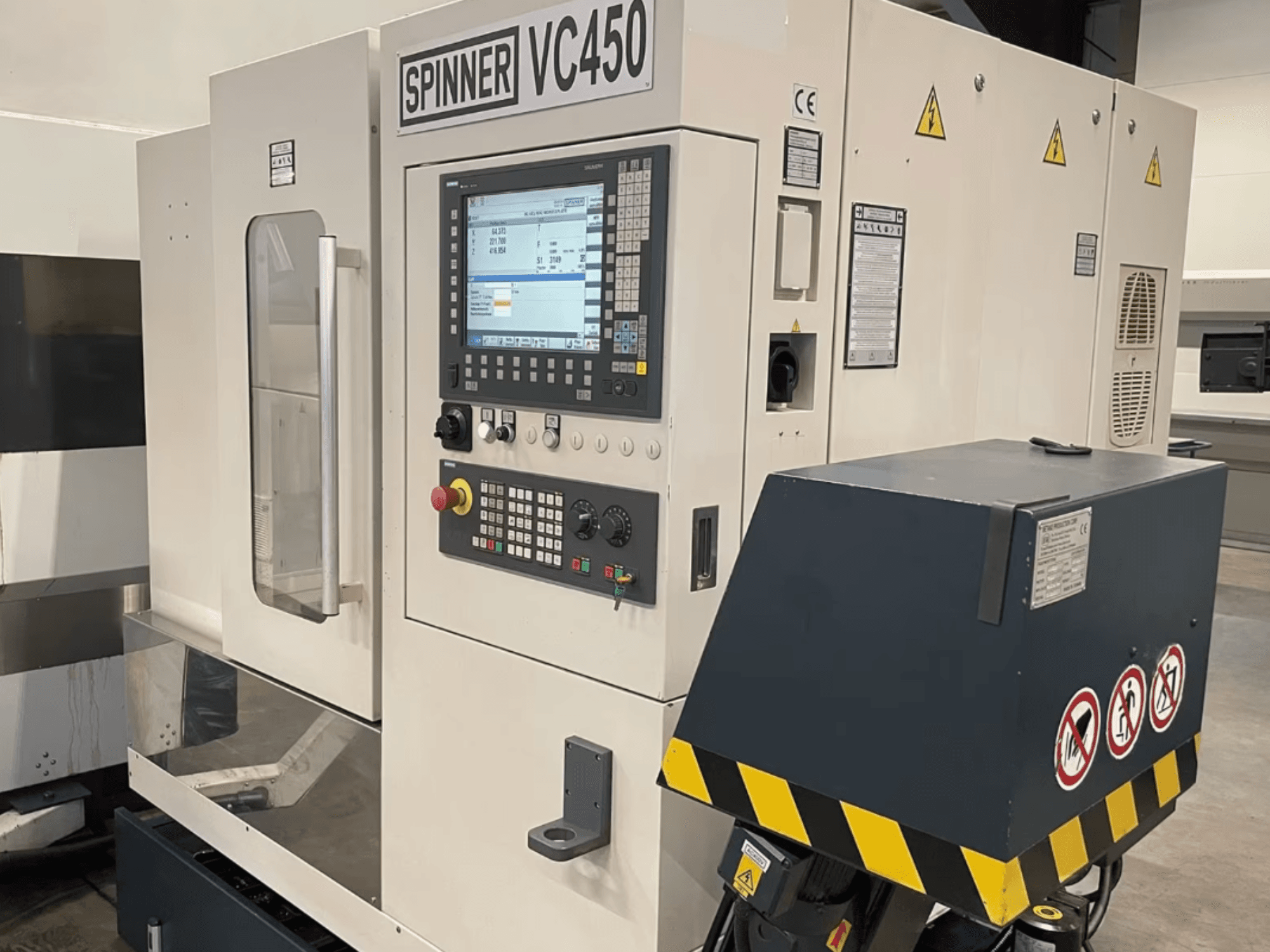 Front view of SPINNER VC450 vertical machining centre, featuring control panel and safety labels, showcasing operational details.