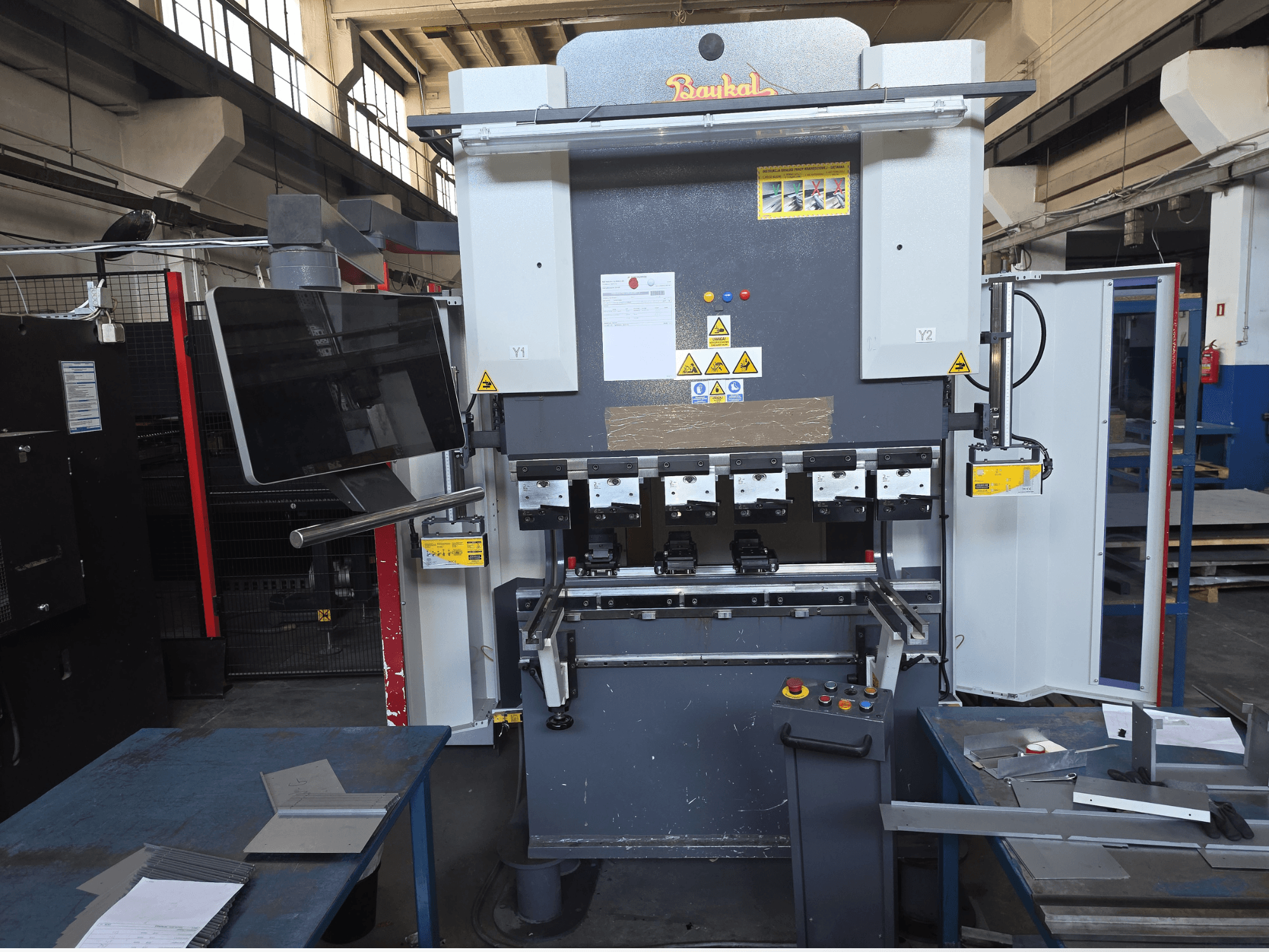 Baykal APHS 125040 press brake, front view, showcasing control panel and safety features with materials on a blue work table.