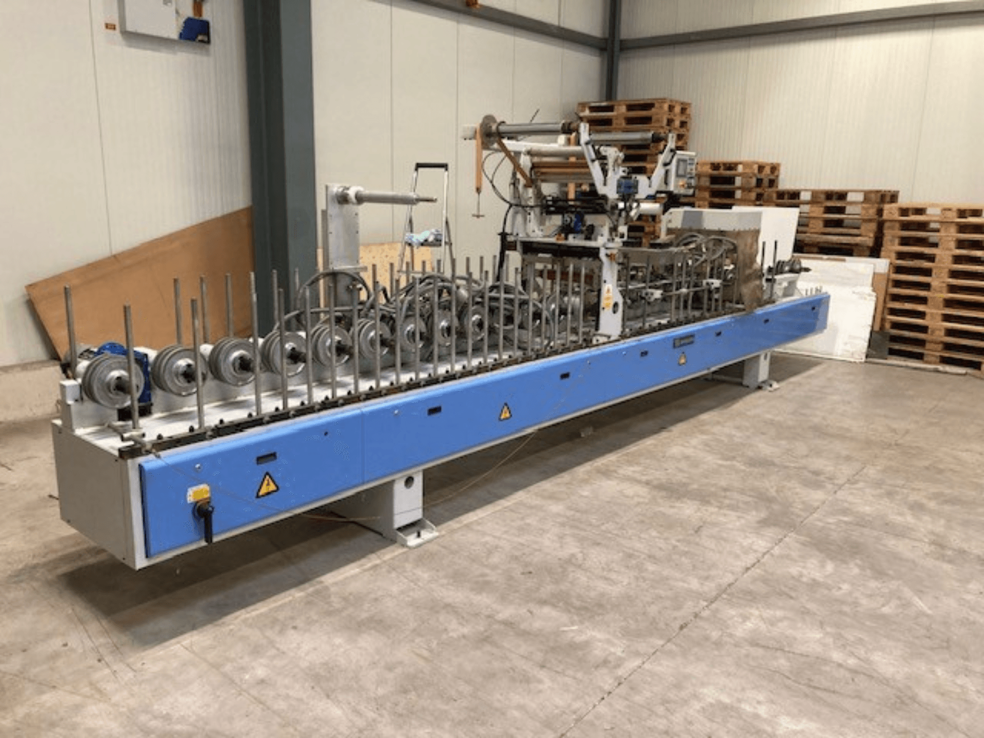 Barberan PUR 46 L laminating press, front view, featuring multiple rollers and a blue base in a warehouse setting.