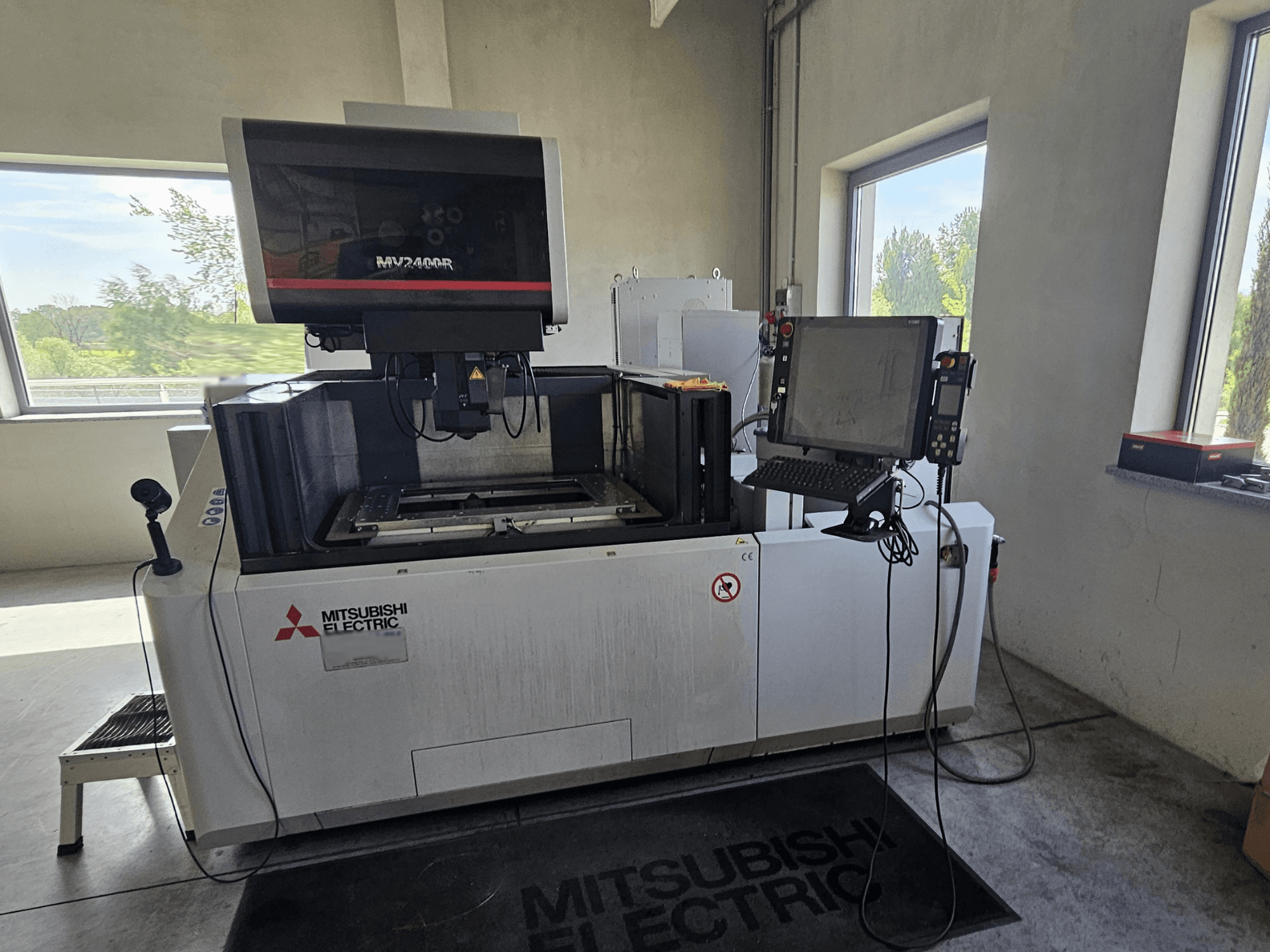 Mitsubishi MV2400R Wire EDM machine in a workshop, featuring a touchscreen control panel and workspace area.