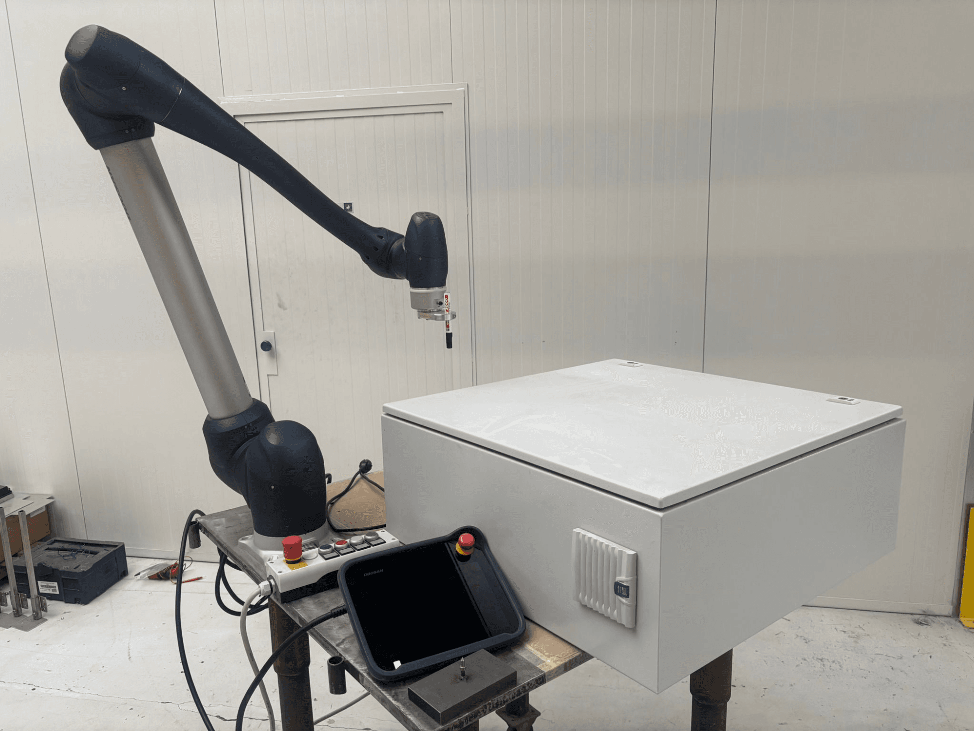 DOOSAN M0617 collaborative robot in side view, with robotic arm extended above a control interface and a white box on a table.