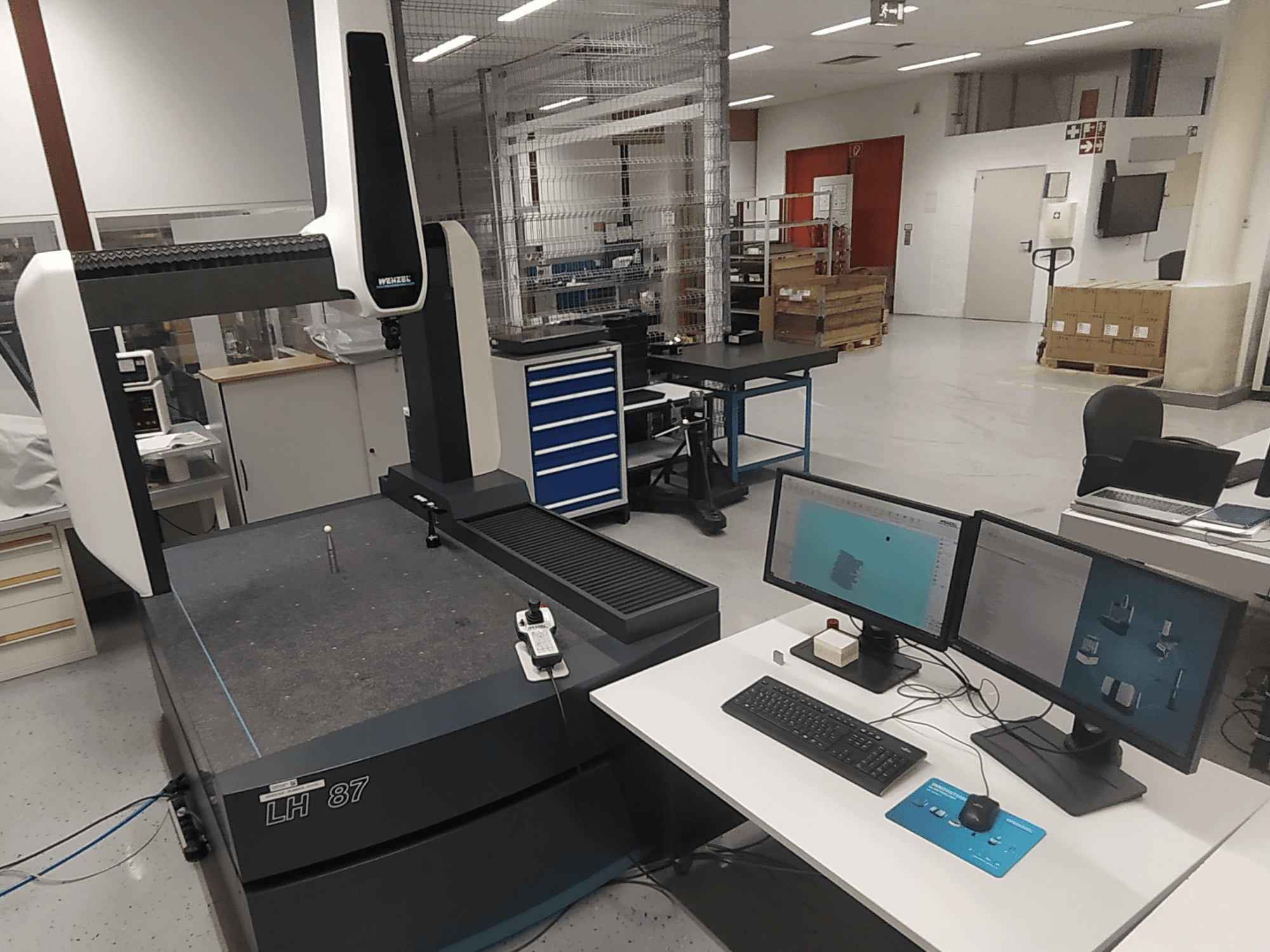 Wenzel LH 87 coordinate measuring machine visible in a lab setting, with dual monitors and measurement probe on the table.