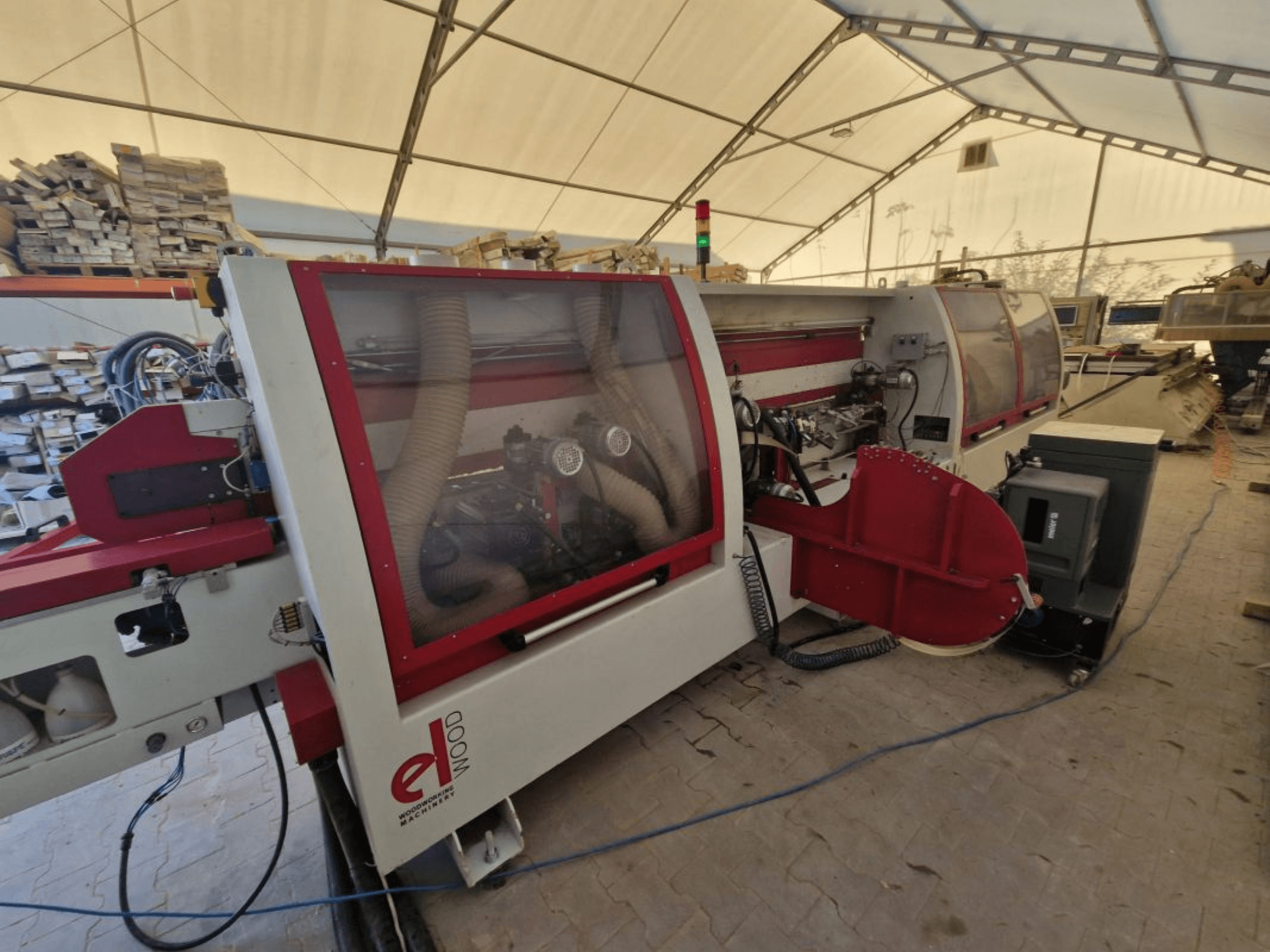 ELWOOD EDL SOFT edgebander, side view showing dust extraction and controls inside a workshop with wood stacks.