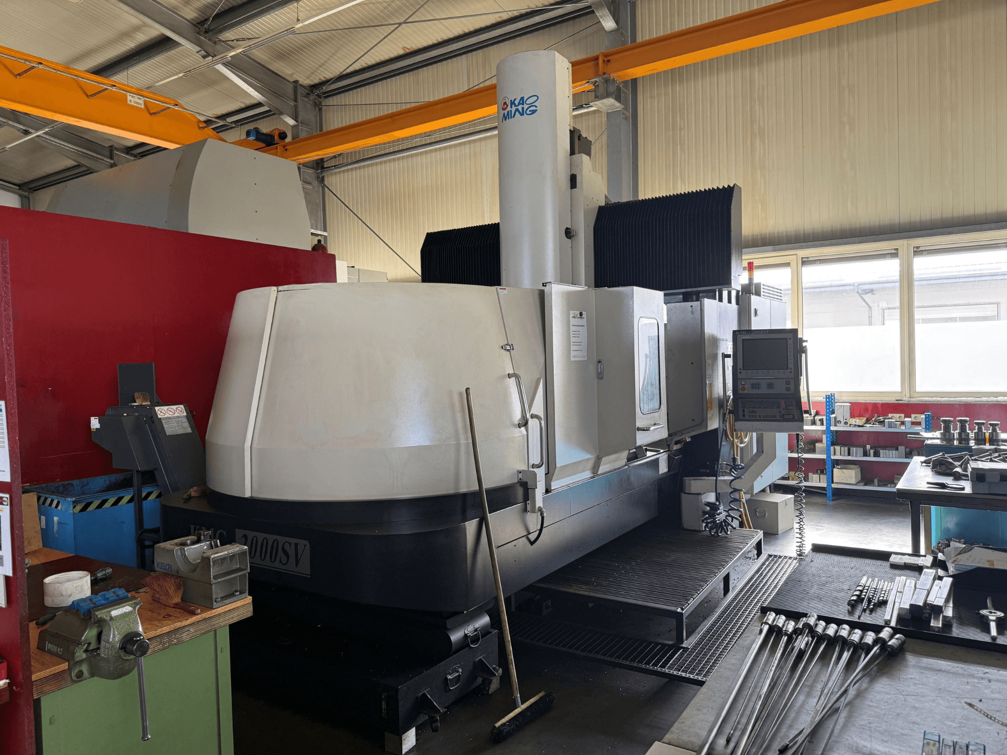 Gantry milling machine KAOMING KMC-2000 SV in a workshop, front view with control panel and surrounding tools visible.