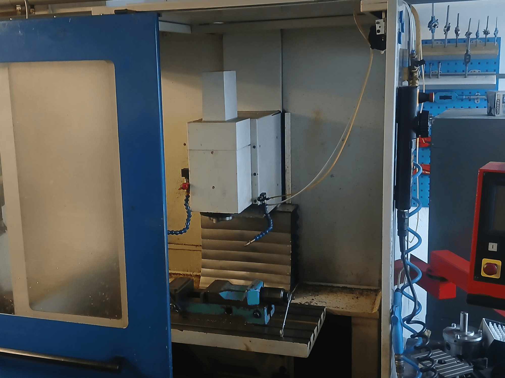 Vertical Machining Centre MACMON M 454 V viewed from the front, showcasing the spindle and machining area with tools nearby.