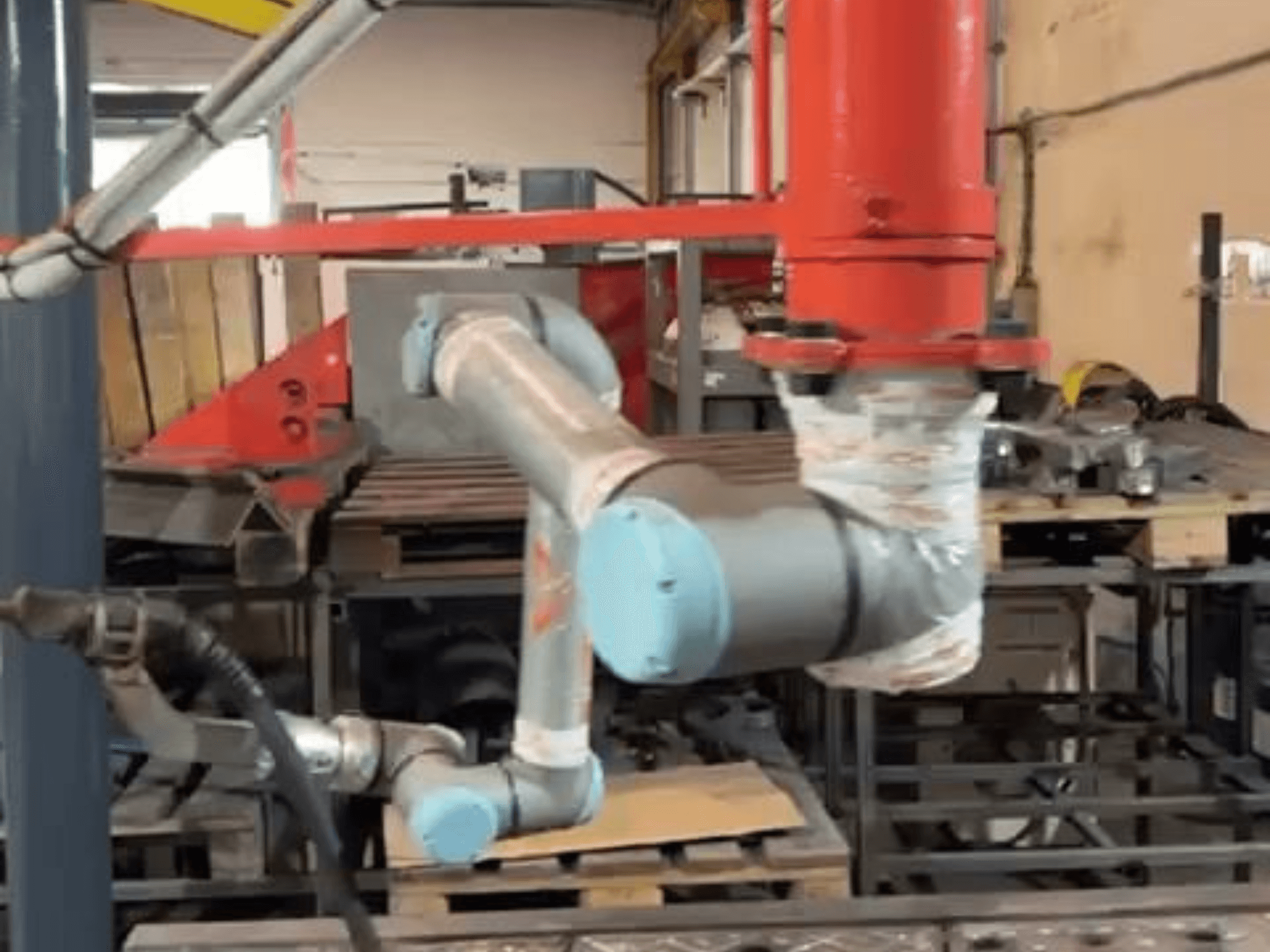 Universal Robots UR10e collaborative robot in a workshop, side view showing arm and joint movements near machinery.
