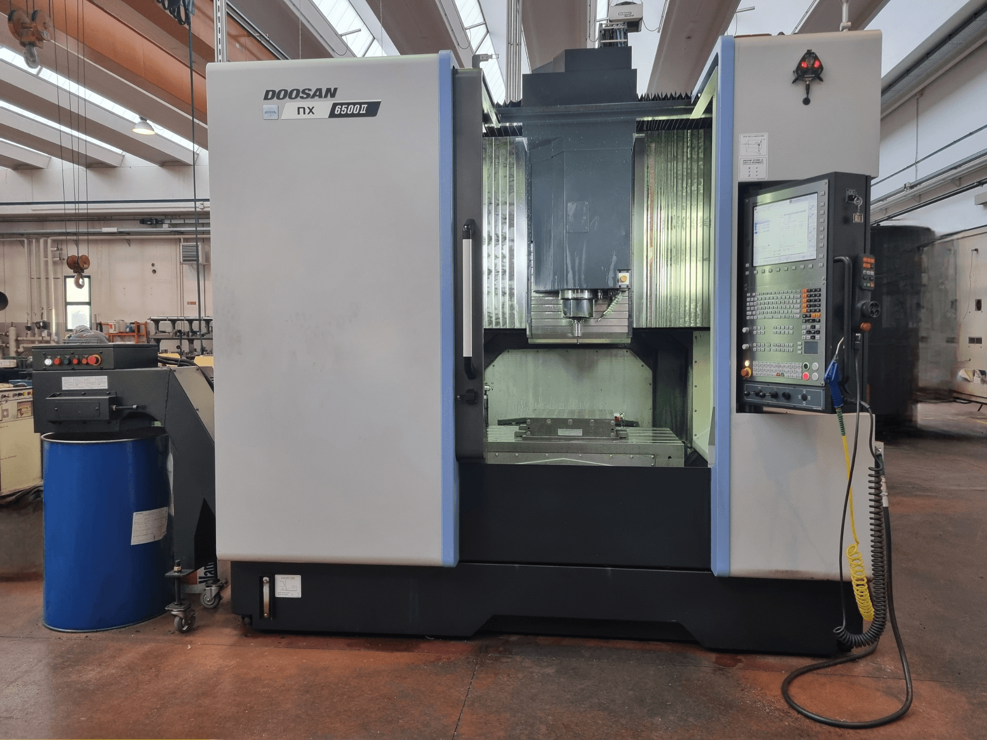 Doosan NX 6500 II CNC machine, front view, featuring control panel and machining area, positioned beside a blue barrel.