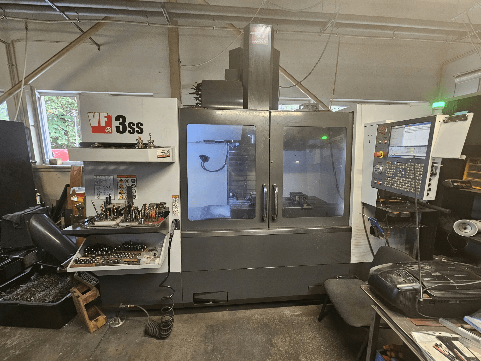 Haas VF-3SS vertical machining center in a workshop, front view showing control panel and tool storage compartment.