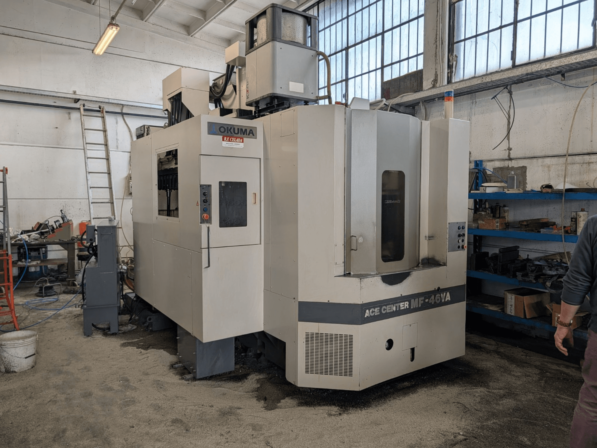 Okuma ACE CENTER MF-46VA vertical machining centre in a workshop, showing front view with control panel and surrounding equipment.