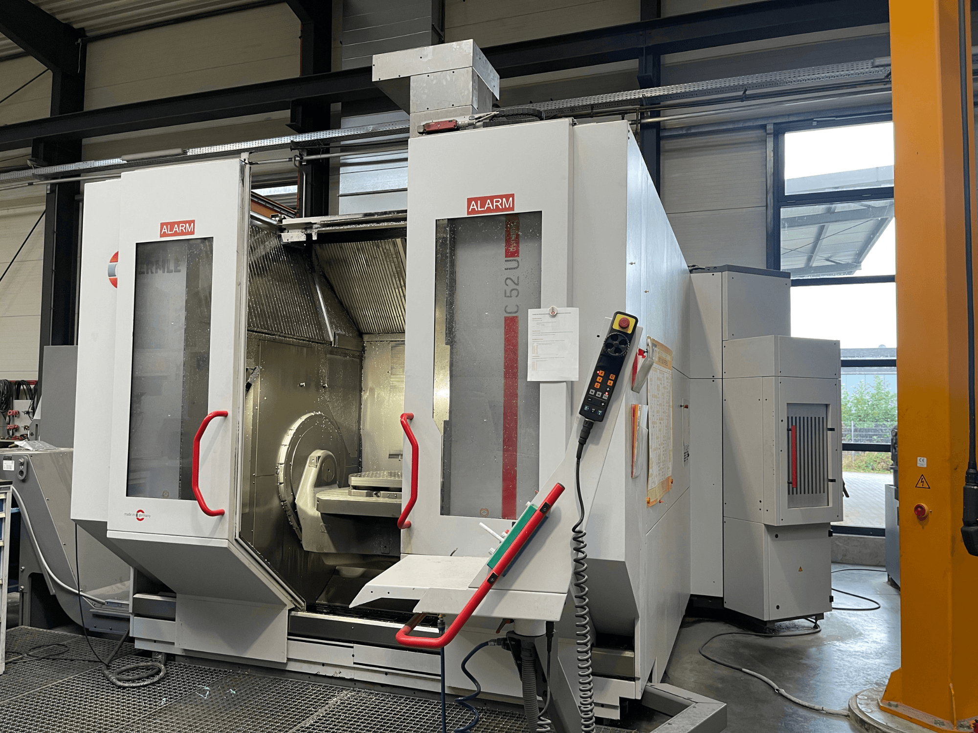 HERMLE C 52 U vertical machining center in a workshop, front view showing open doors and control panel with buttons.