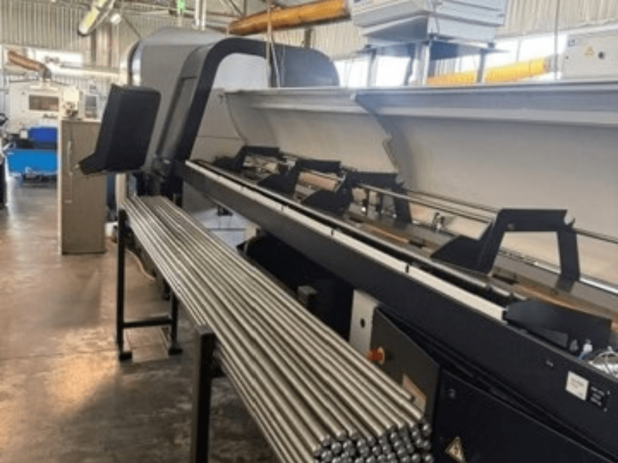Front view of TORNOS EvoDECO 32 Swiss Type Turning Machine with metal rods aligned beside it, showcasing industrial workspace.