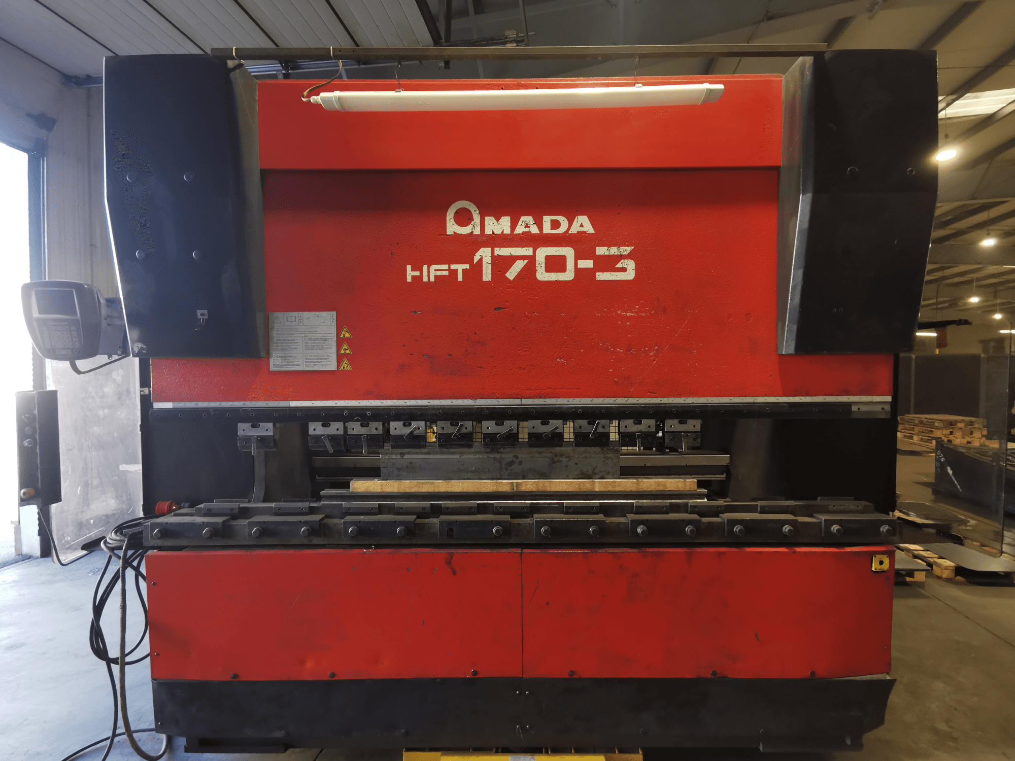 Red Amada HFT 170-3 press brake viewed from the front, showing control panel, bending tools, and work surface.