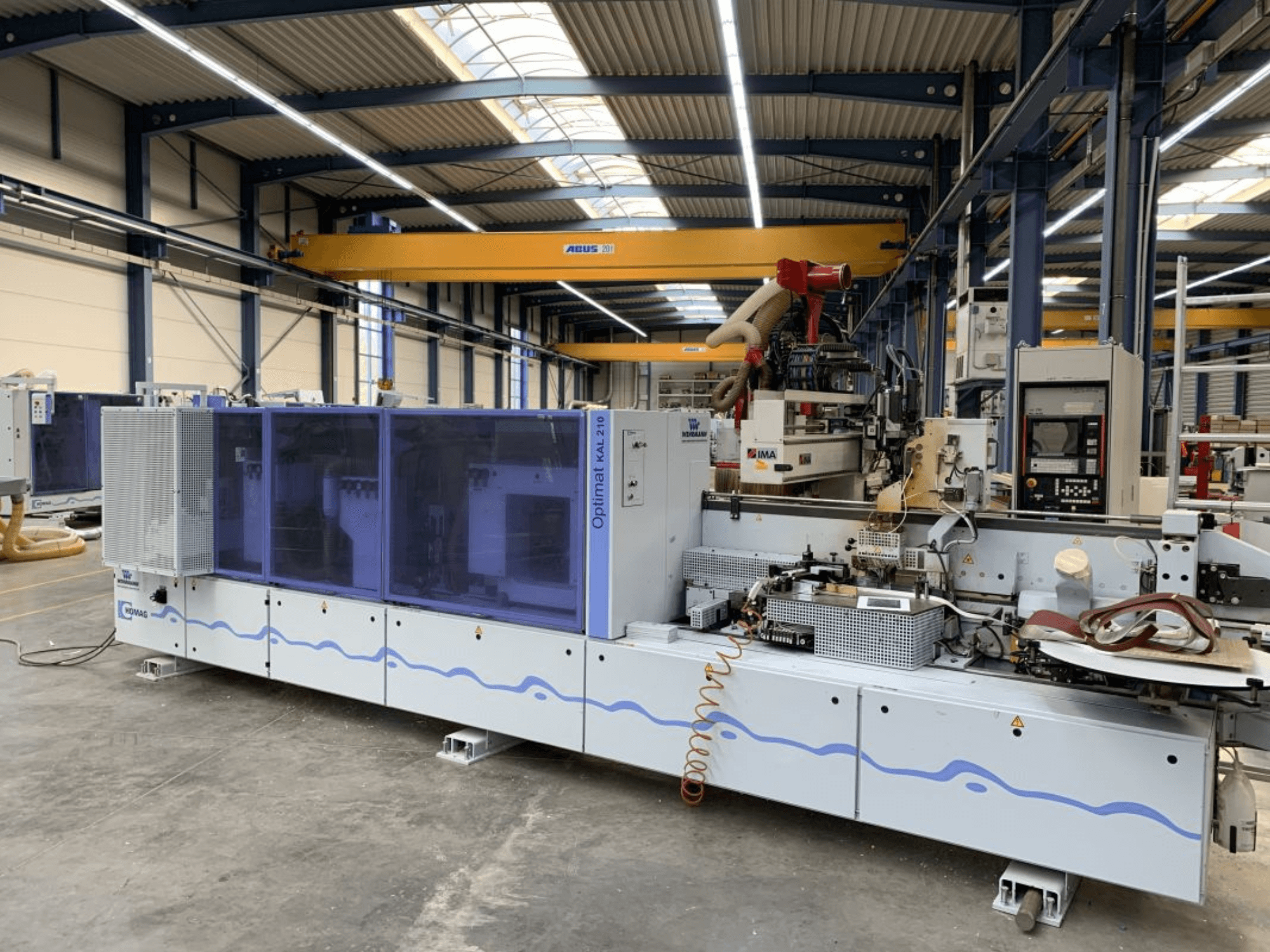 HOMAG Optimat KAL210 edgebander in a front view, showcasing its control panel and processing area in a factory setting.