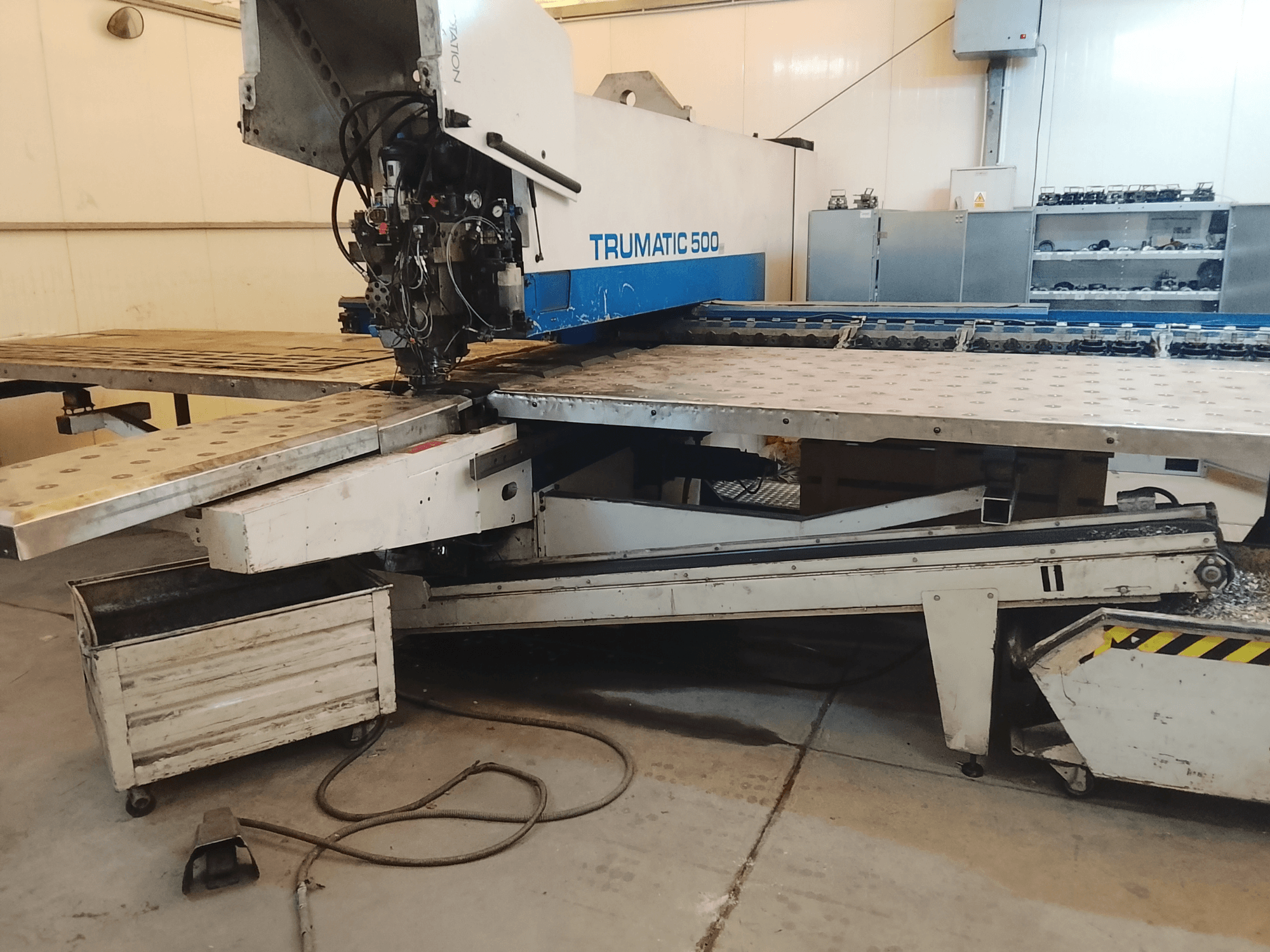 TRUMATIC 500 CNC machine in a workshop, side view showing cutting head and metal worktable with pre-drilled holes.