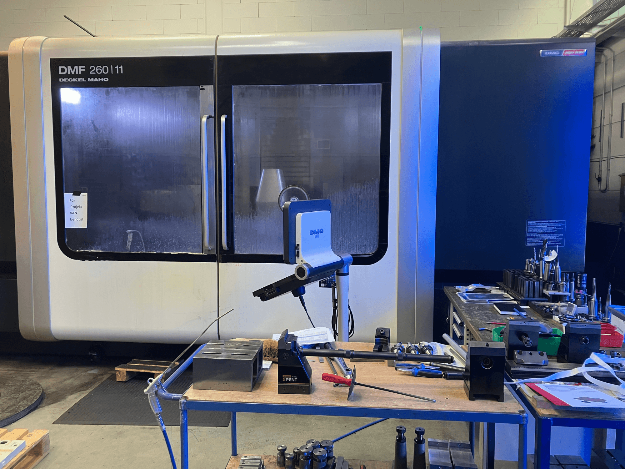 Front view of DMG DECKEL MAHO DMF 260|11 vertical machining center with tools and materials on a workstation.