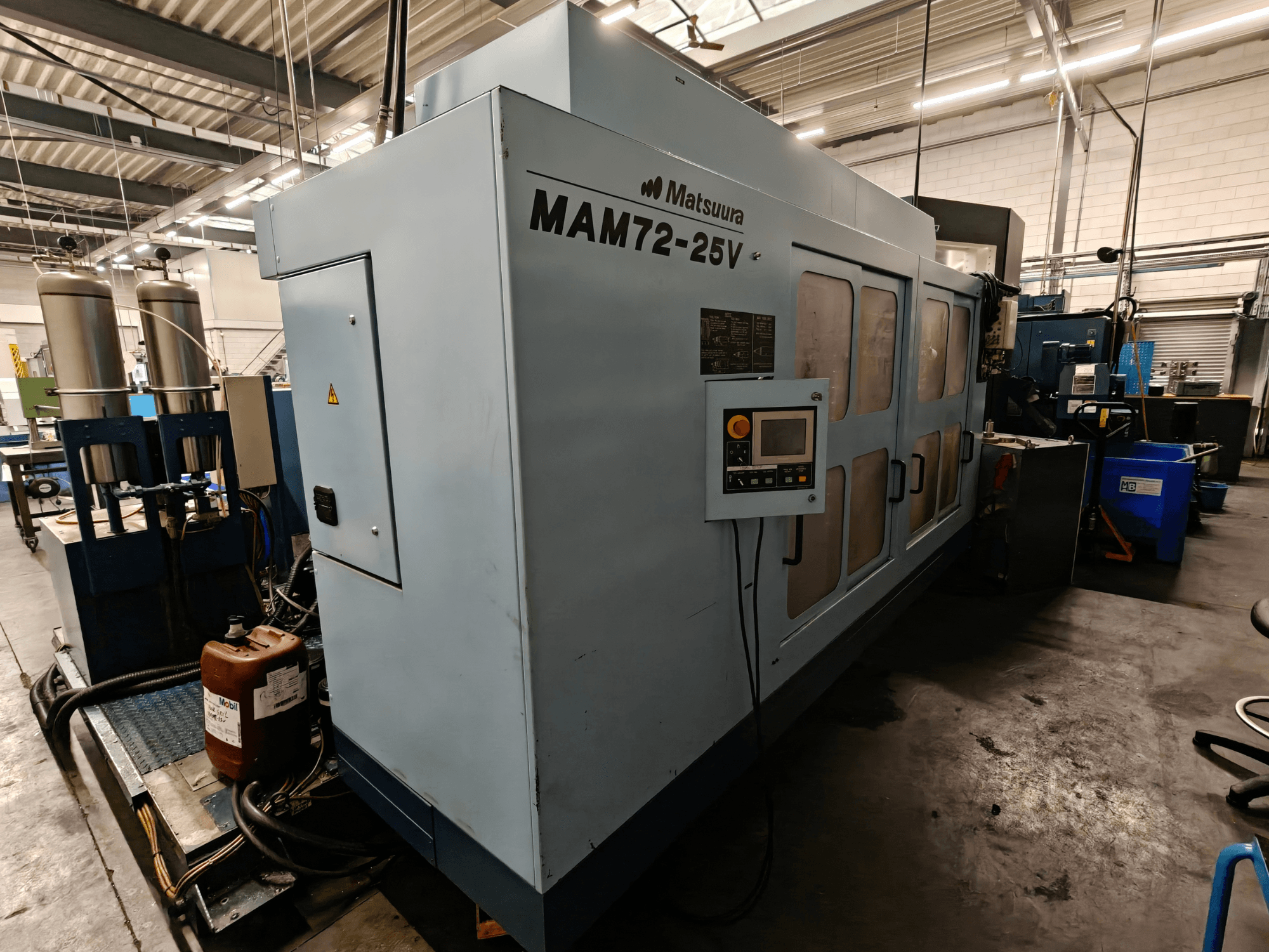 Matsuura MAM72-25V CNC machine, side view, features control panel, dual coolant tanks, and workspace in an industrial setting.