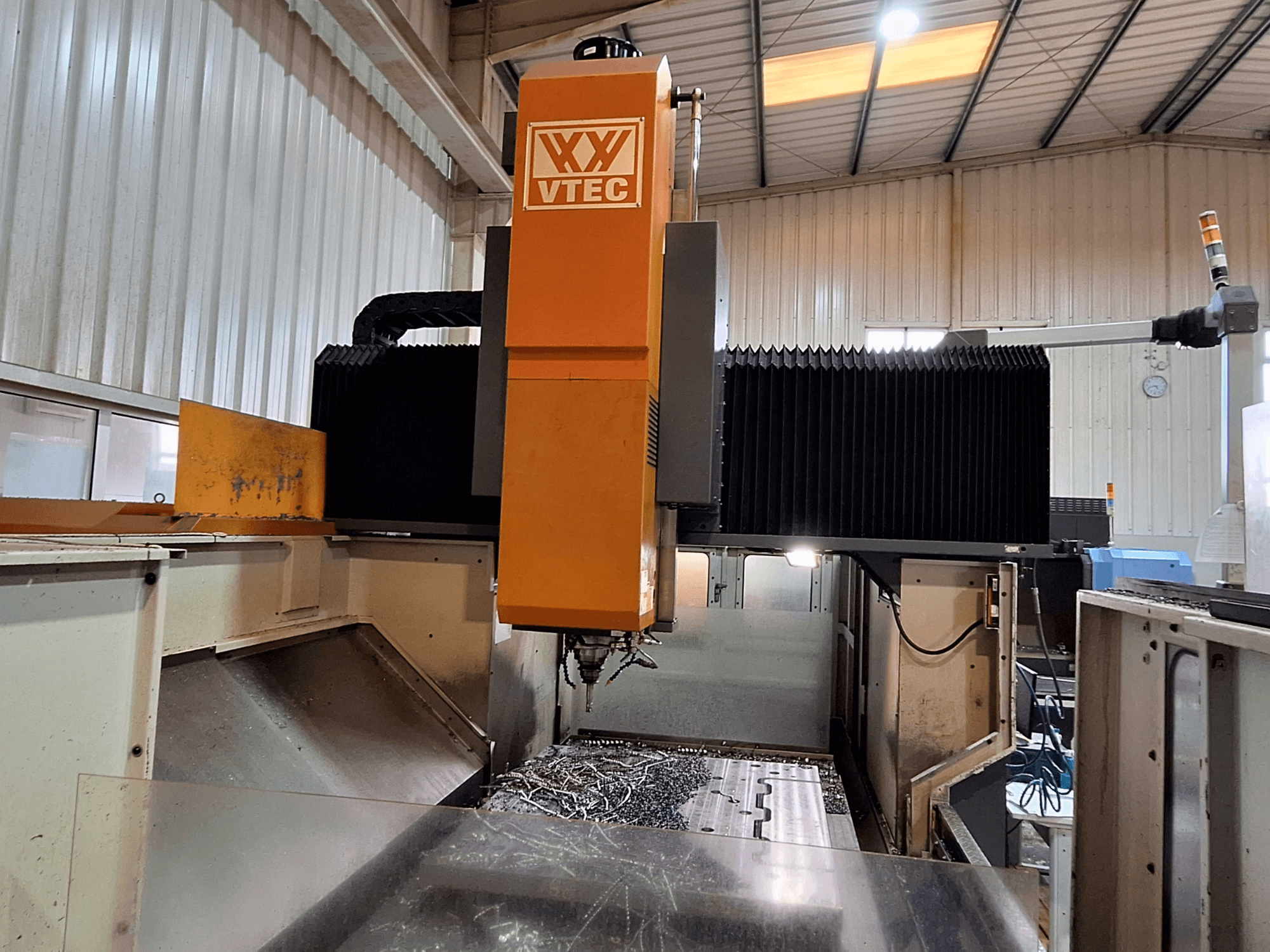 Gantry milling machine by PORTIC, model VTEC, shown from the front view with cutting tool and metal shavings visible.