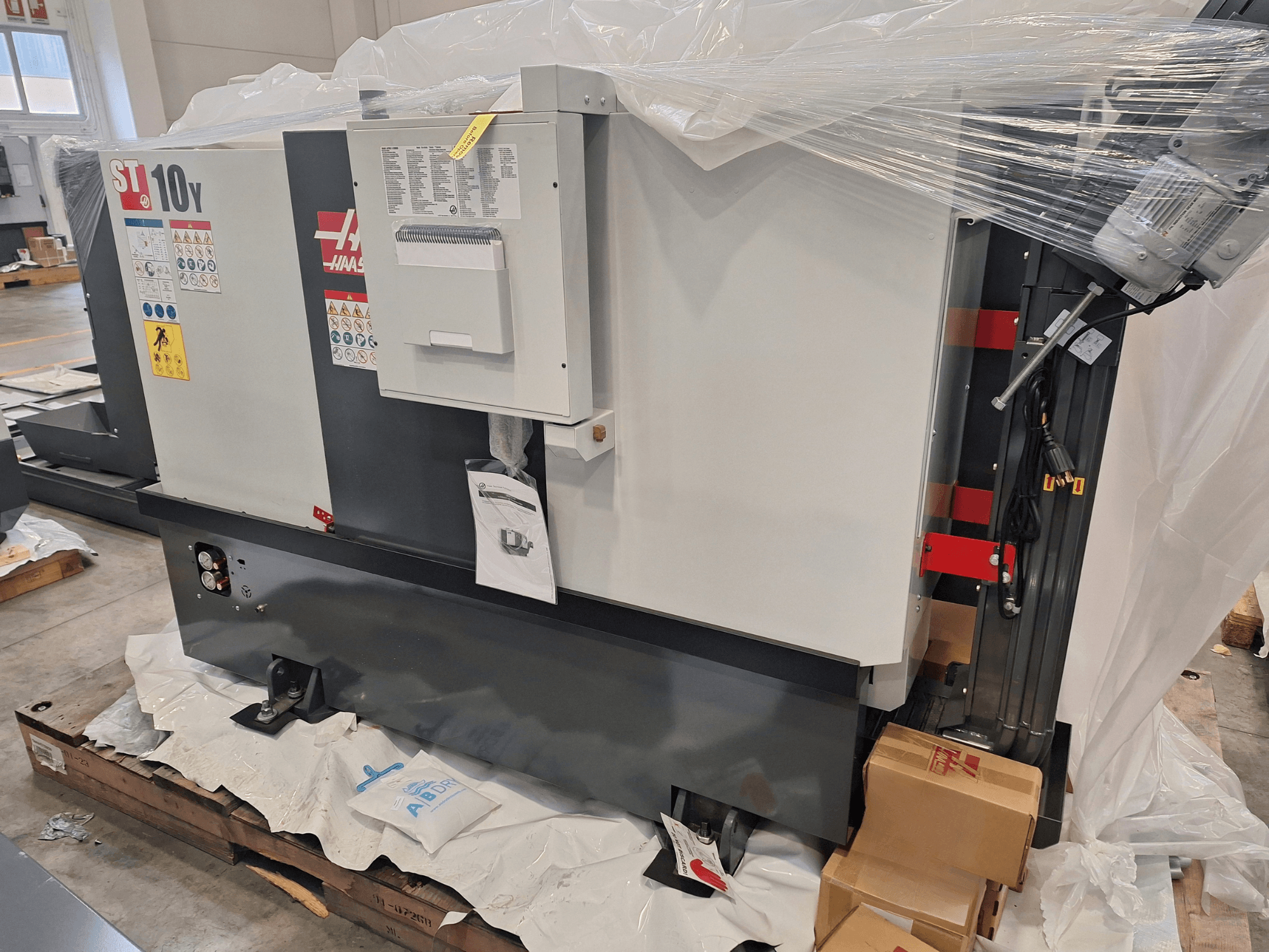 HAAS ST-10Y EU horizontal turning machine side view, wrapped in plastic, with control panel and warning labels visible.