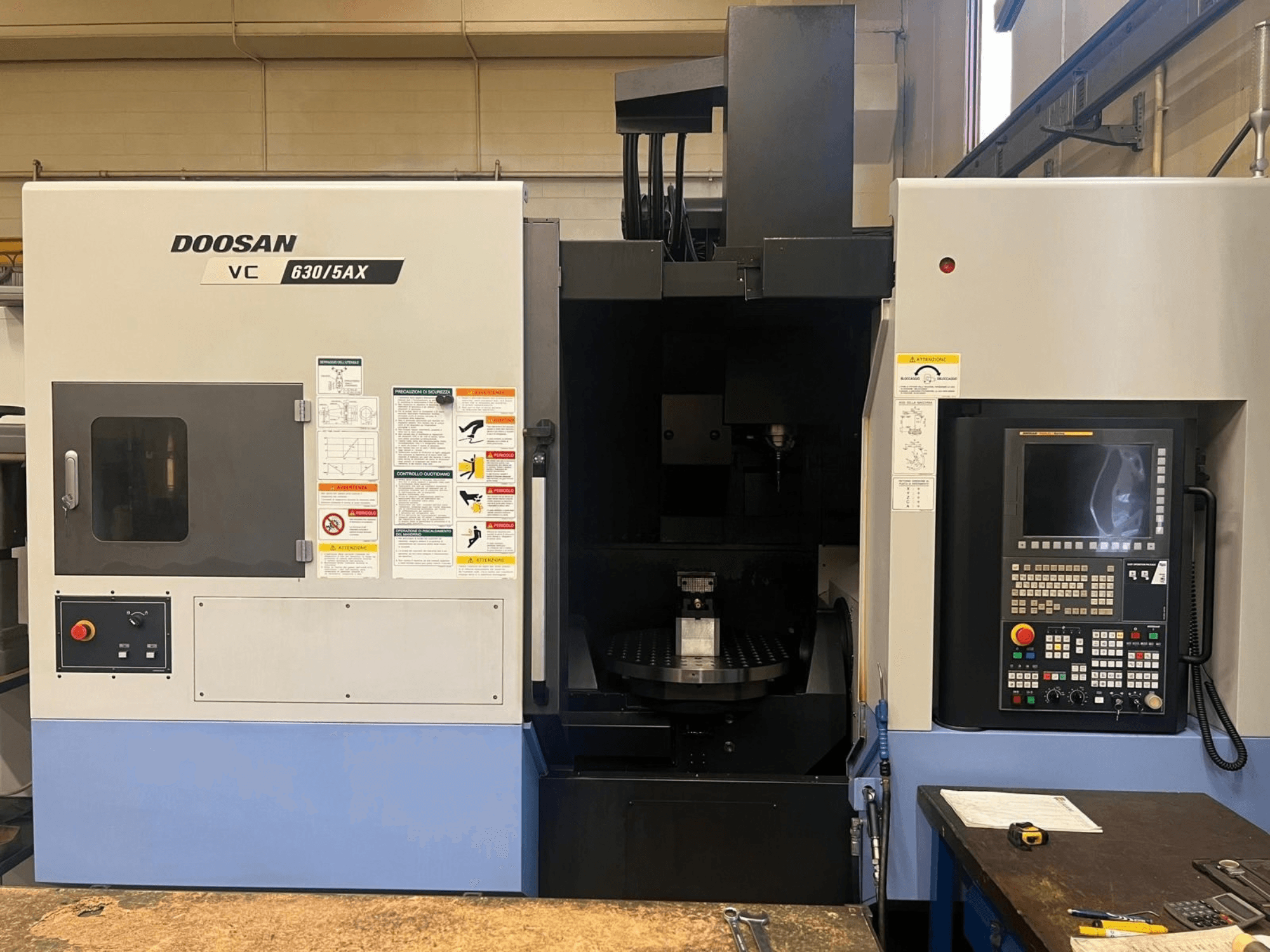 Front view of a DOOSAN VC 630/5AX vertical machining center, showcasing control panel and spindle area with visible safety labels.