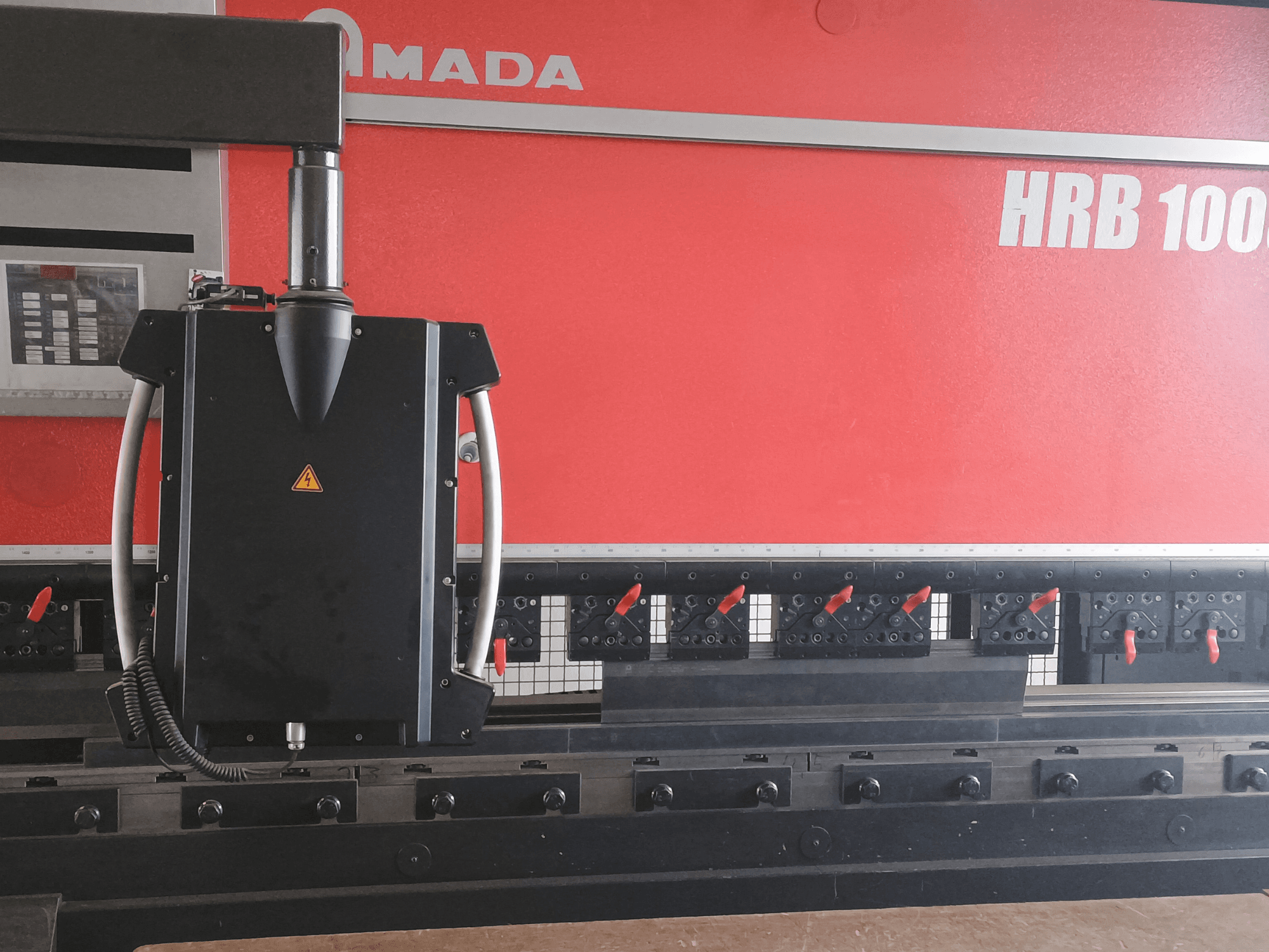 Amada HRB 100 bending machine front view; features a black control head with a conical nozzle and adjustable clamps.