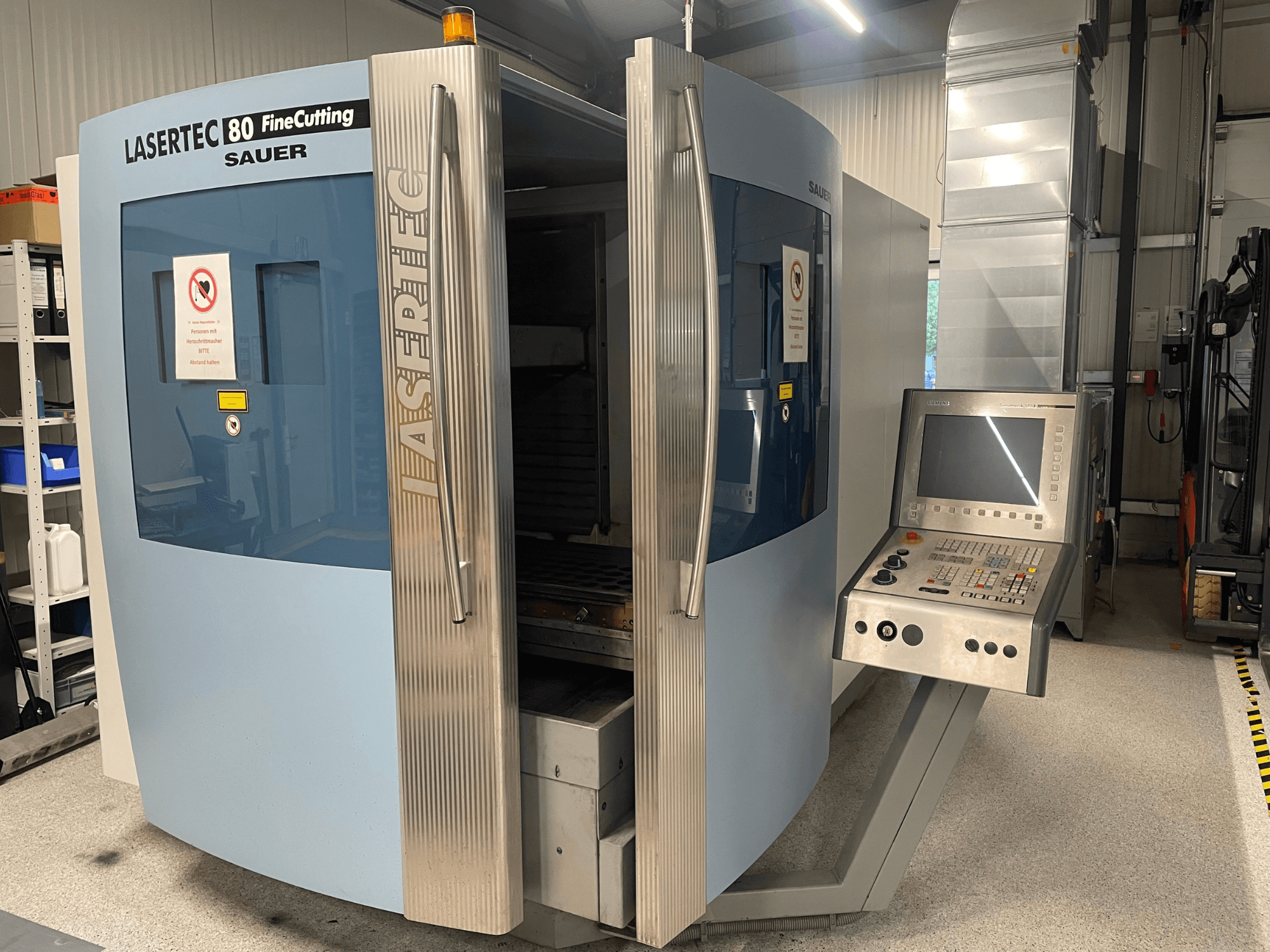 Front view of DMG Sauer Lasertec80 FineCutting sheet metal machine with control panel, doors open, and visible safety signage.