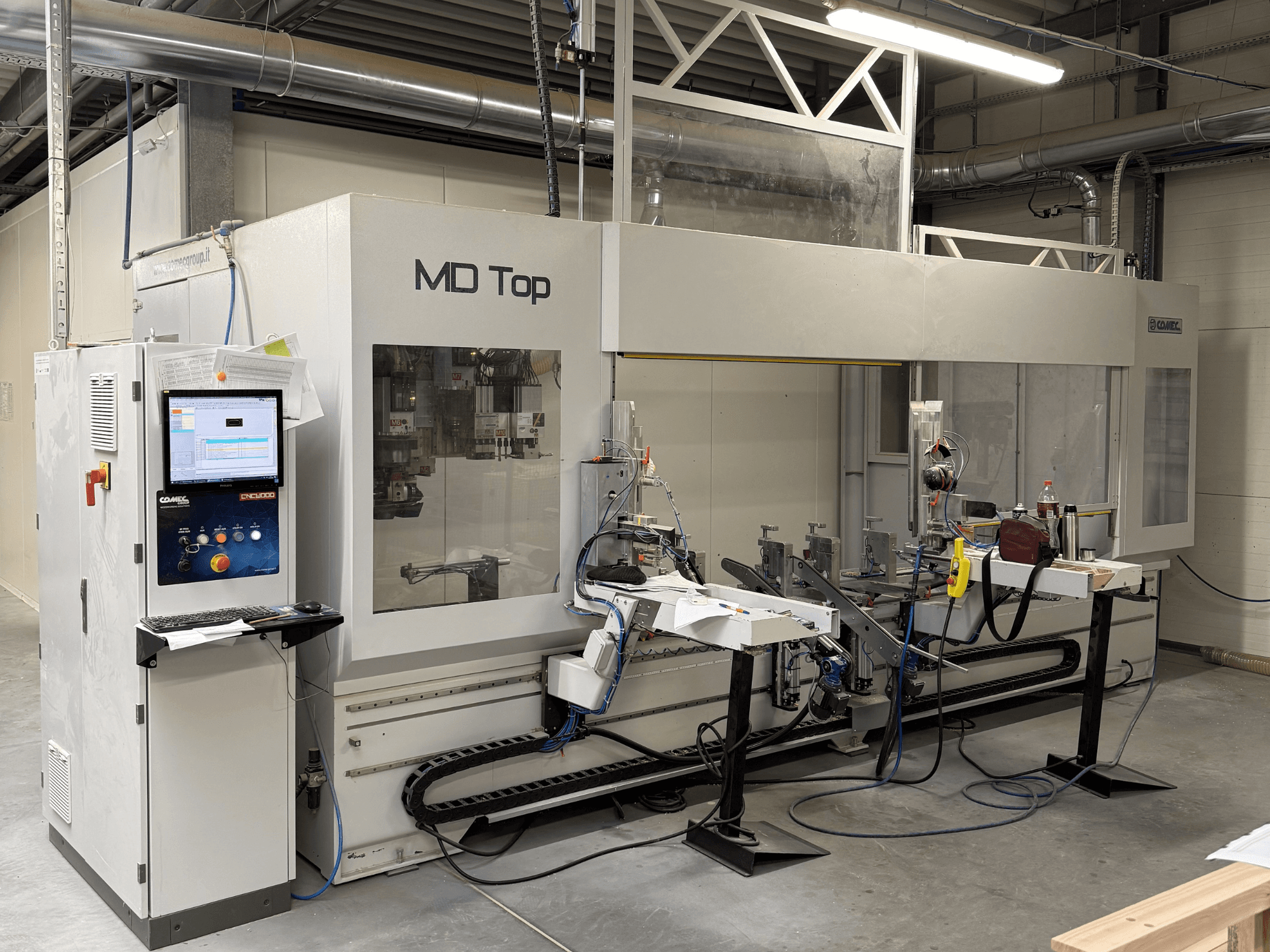MD Top CNC machine viewed from the front, featuring a control panel, robotic arms, and workspace with tools and materials.