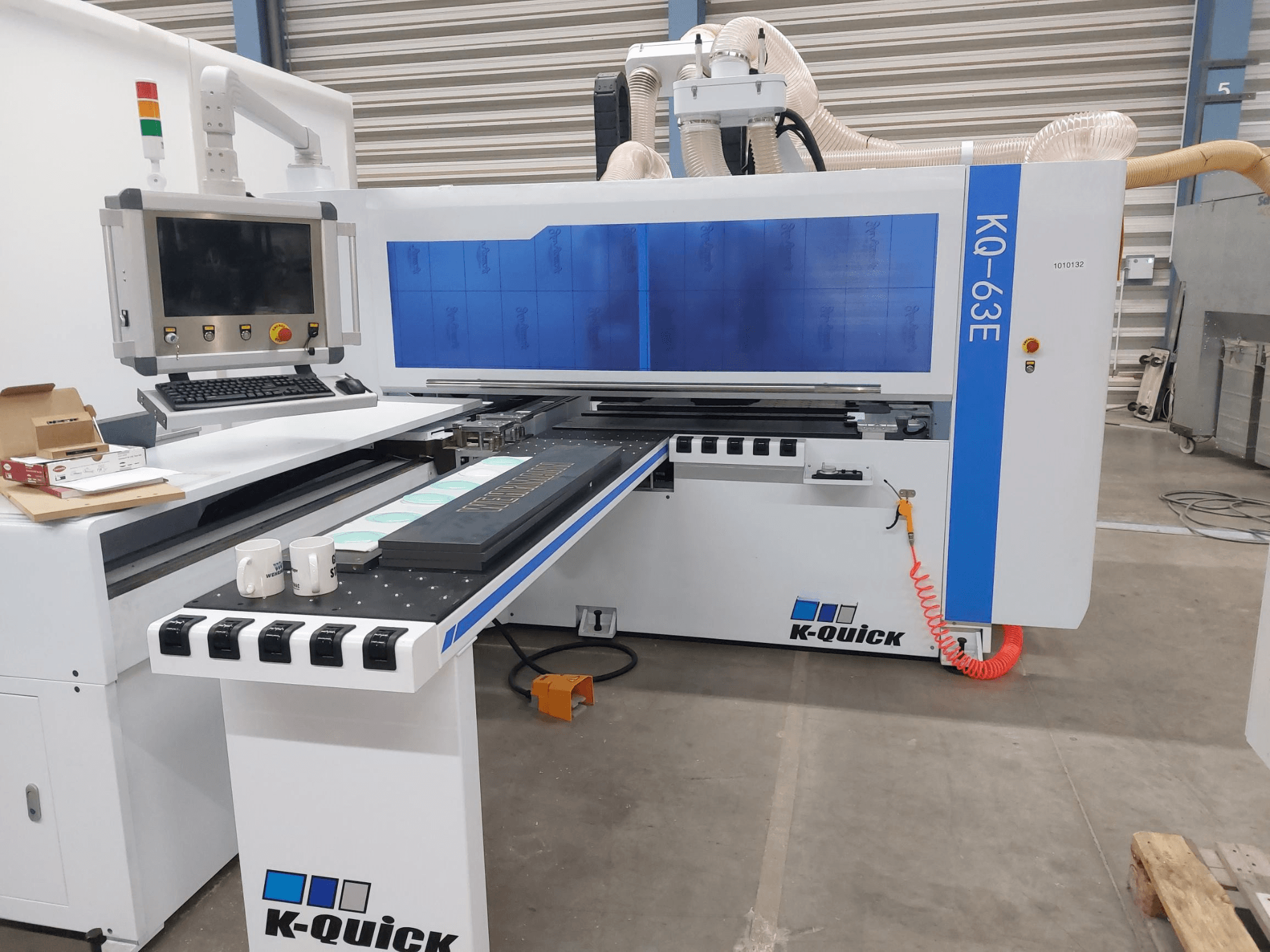 K-Quick KQ-63E CNC machine viewed from the front, featuring a control panel, flatbed, and visible tool placement.