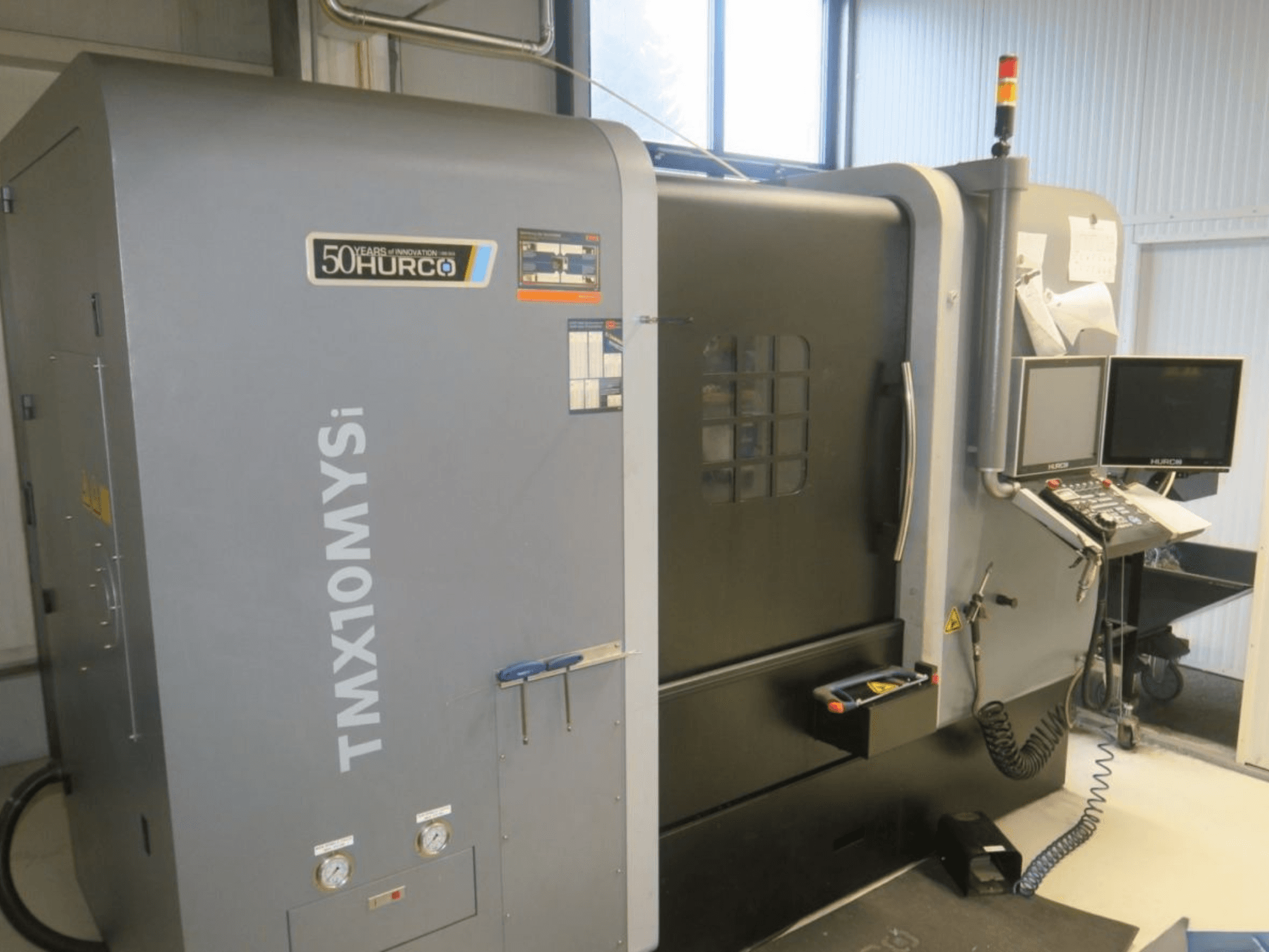 Hurco TMX10MYSi CNC machine in side view; features control panel, emergency lights, and gauges displayed.