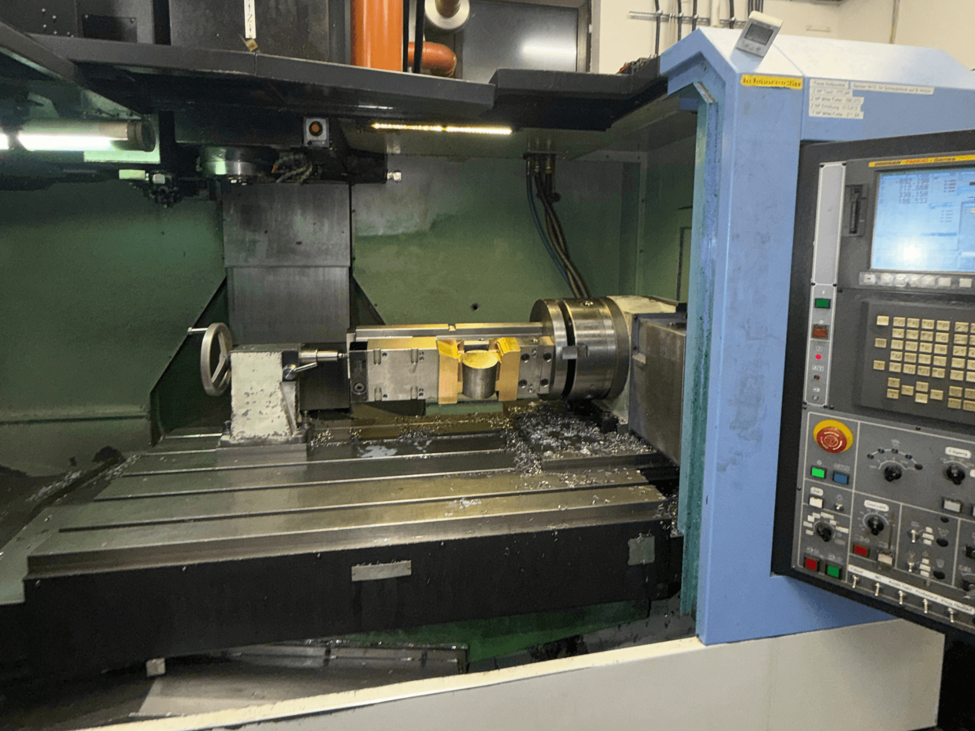 DOOSAN DNM650 Vertical Machining Centre, front view, showcasing the cutting tool and control panel, with metal shavings visible on the table.