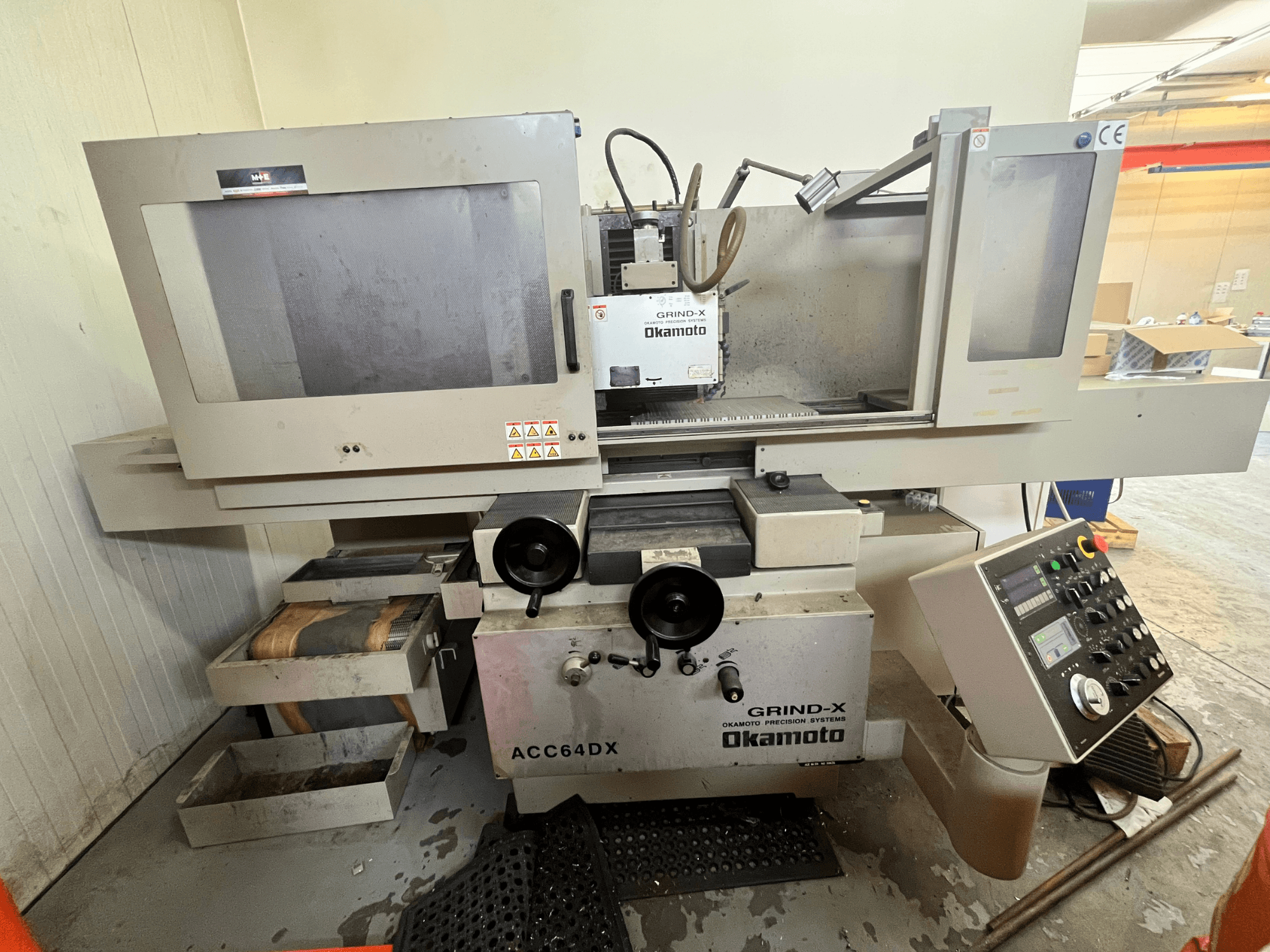 Okamoto ACC64 DX Surface Grinding Machine in front view, showing grinding wheel, control panel, and storage drawers.