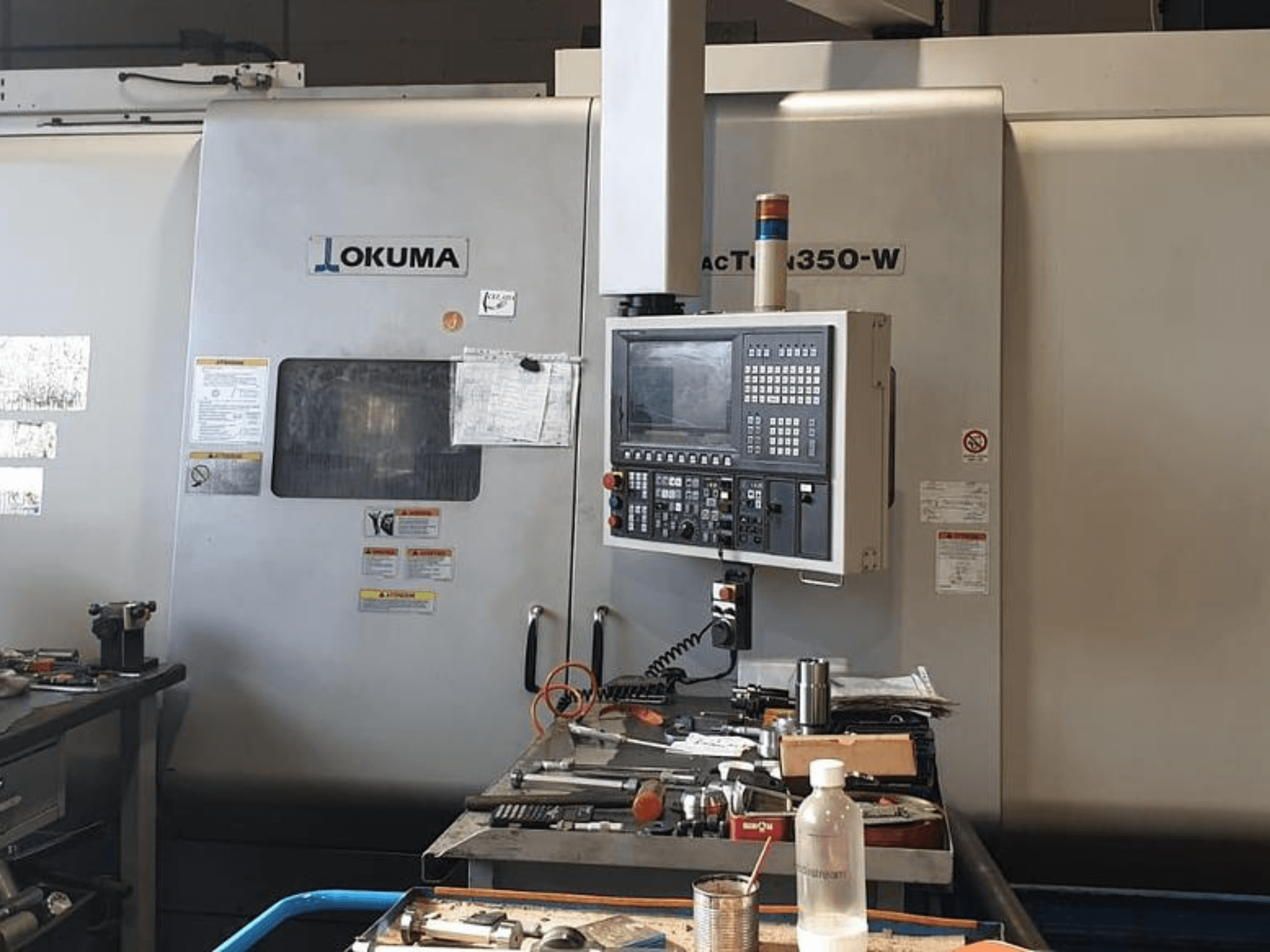Okuma MAC TURN 350-W turn-mill center, front view with control panel and workspace cluttered with tools and a bottle.