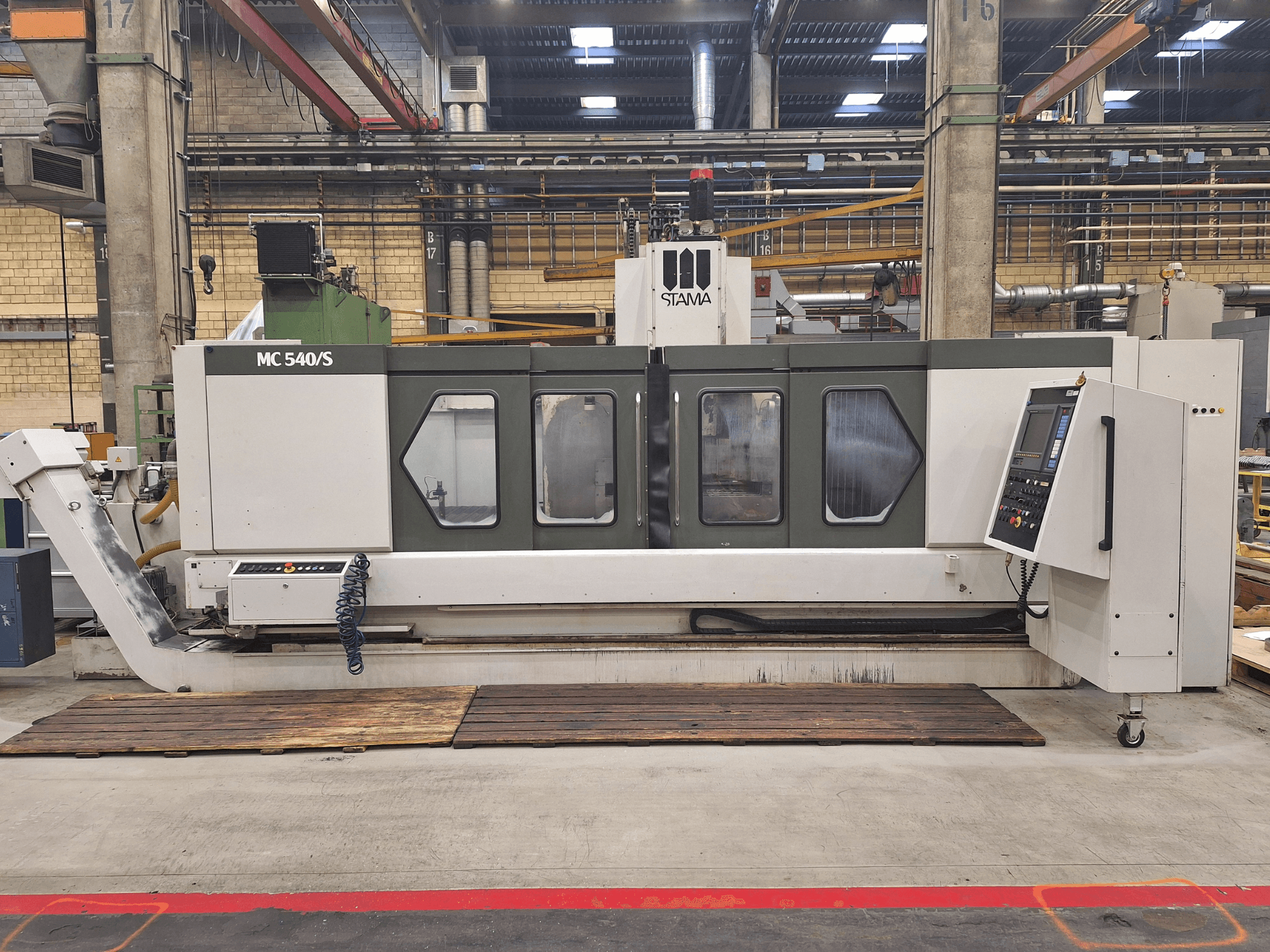 STAMA MC 540S vertical machining centre in a factory, front view, showcasing control panel and milling area with wooden planks.