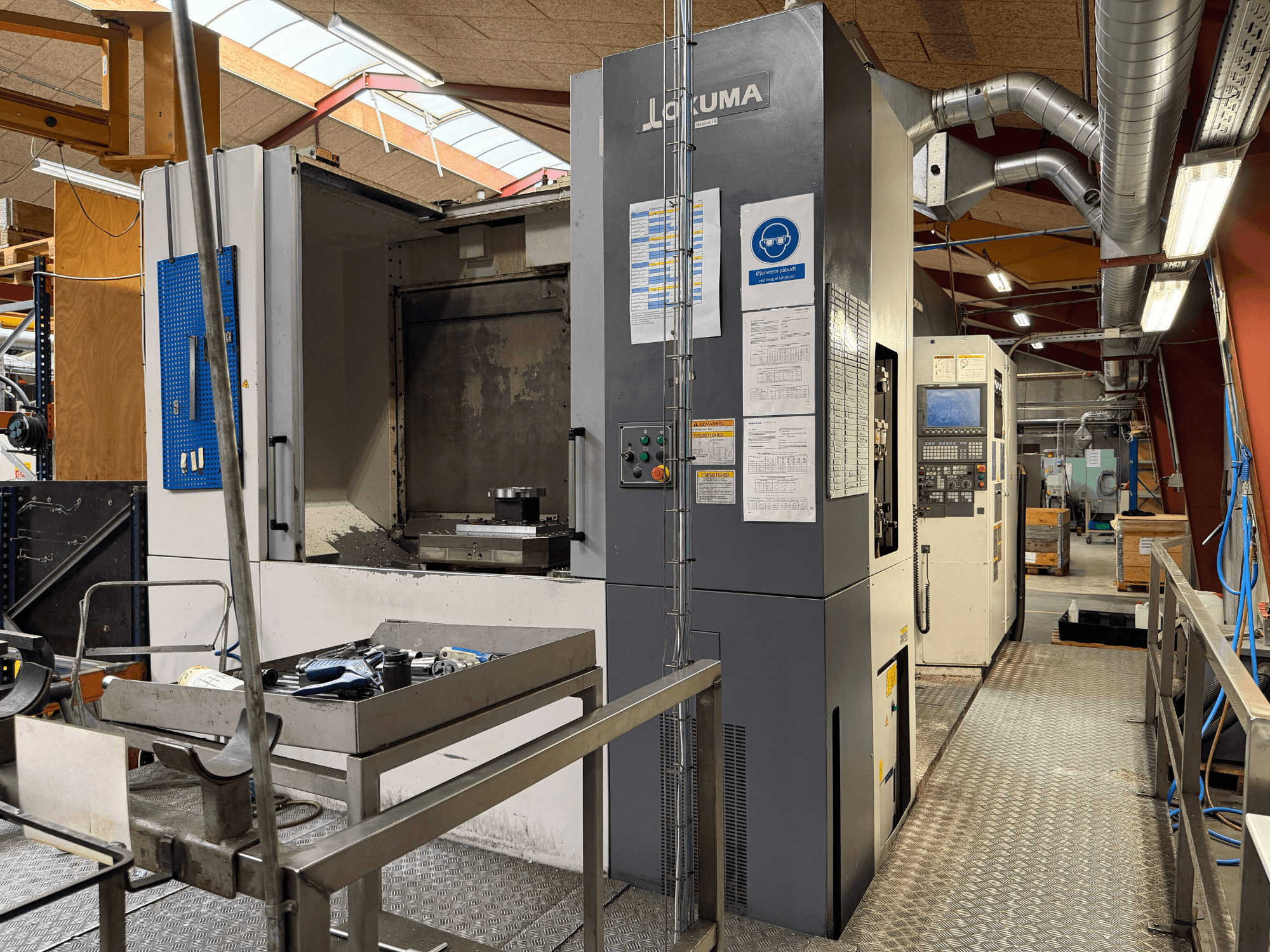 Okuma MA-600HB horizontal machining center, front view, showing tools on a metal table and machine controls.