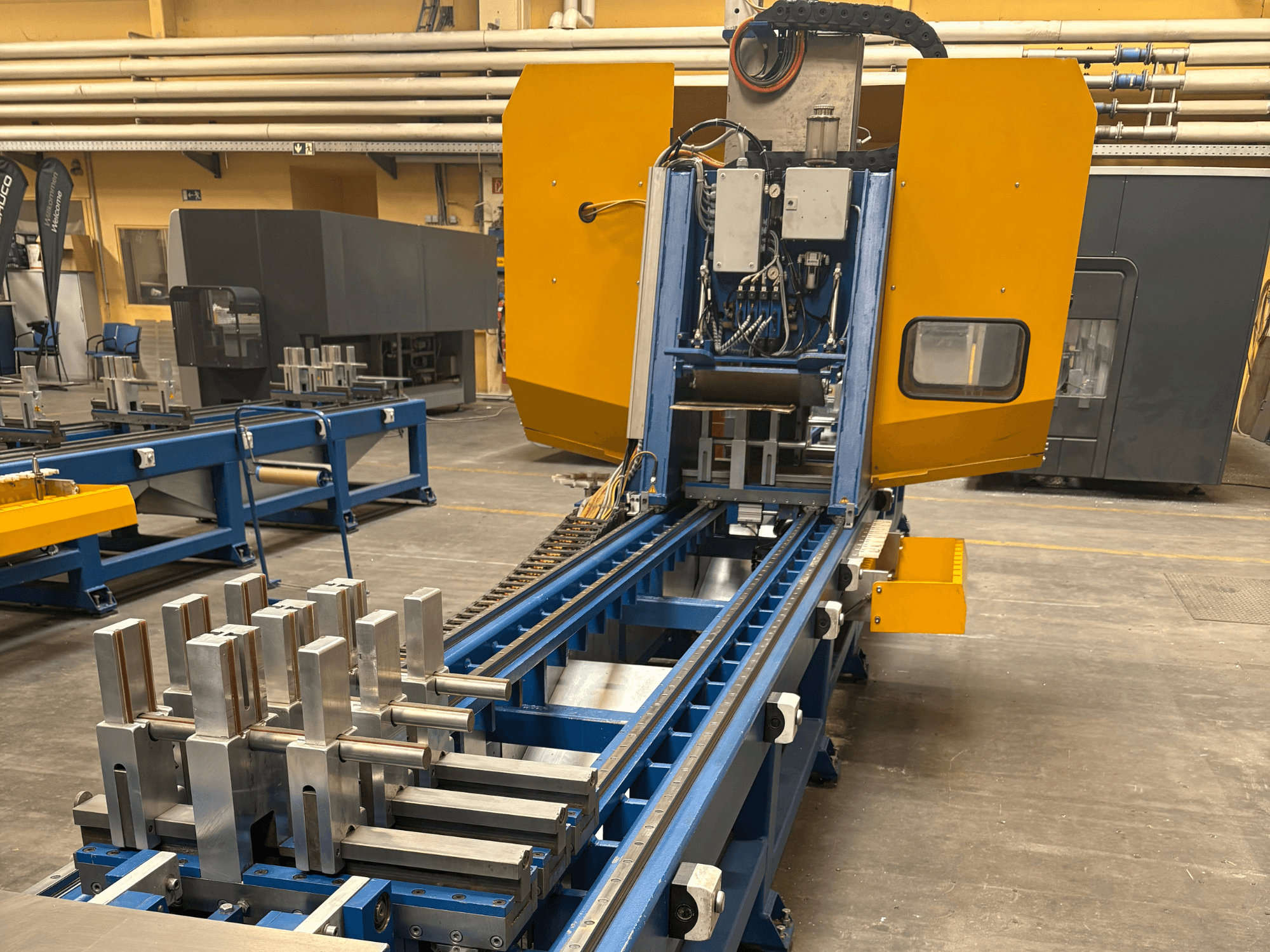 Front view of SCHÜCO PBX AL Universal Machining Centre, showcasing metallic workpieces on a blue machining bed.