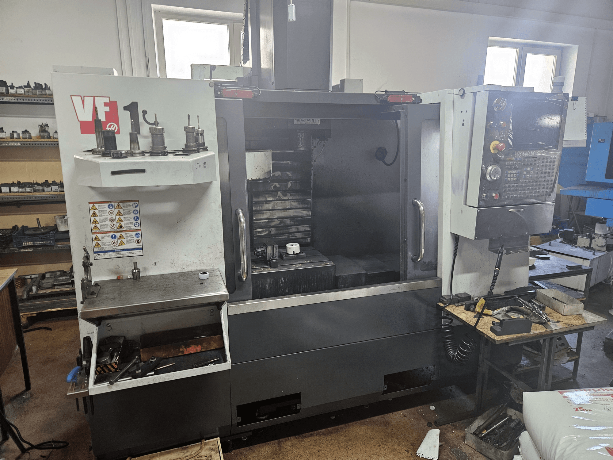 HAAS VF-1 vertical machining center, front view with tools on the side, control panel visible, and workspace in background.