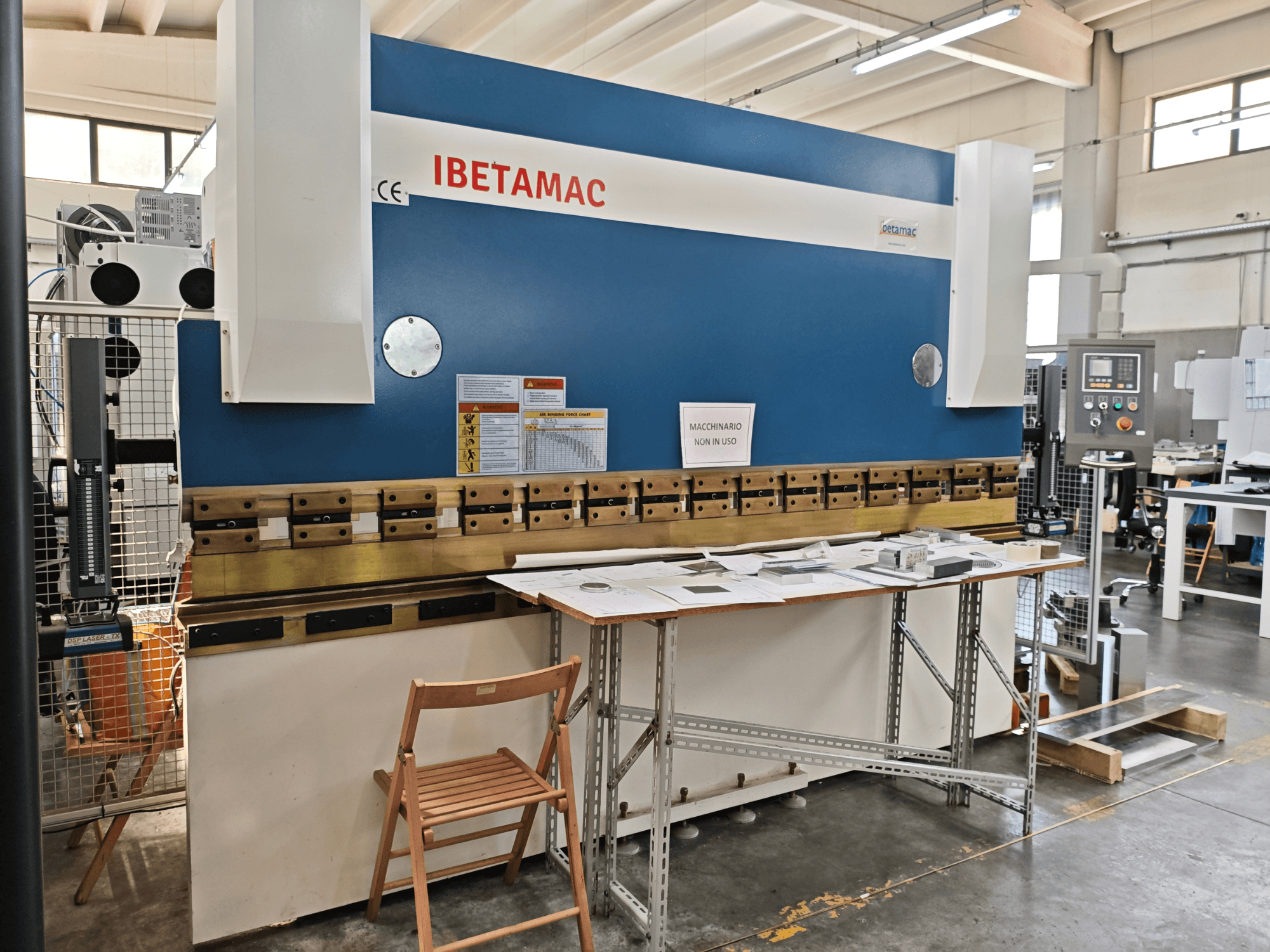 IBETAMAC 3200 100T press brake in a workshop, side view showing control panel, work area, and safety notices.