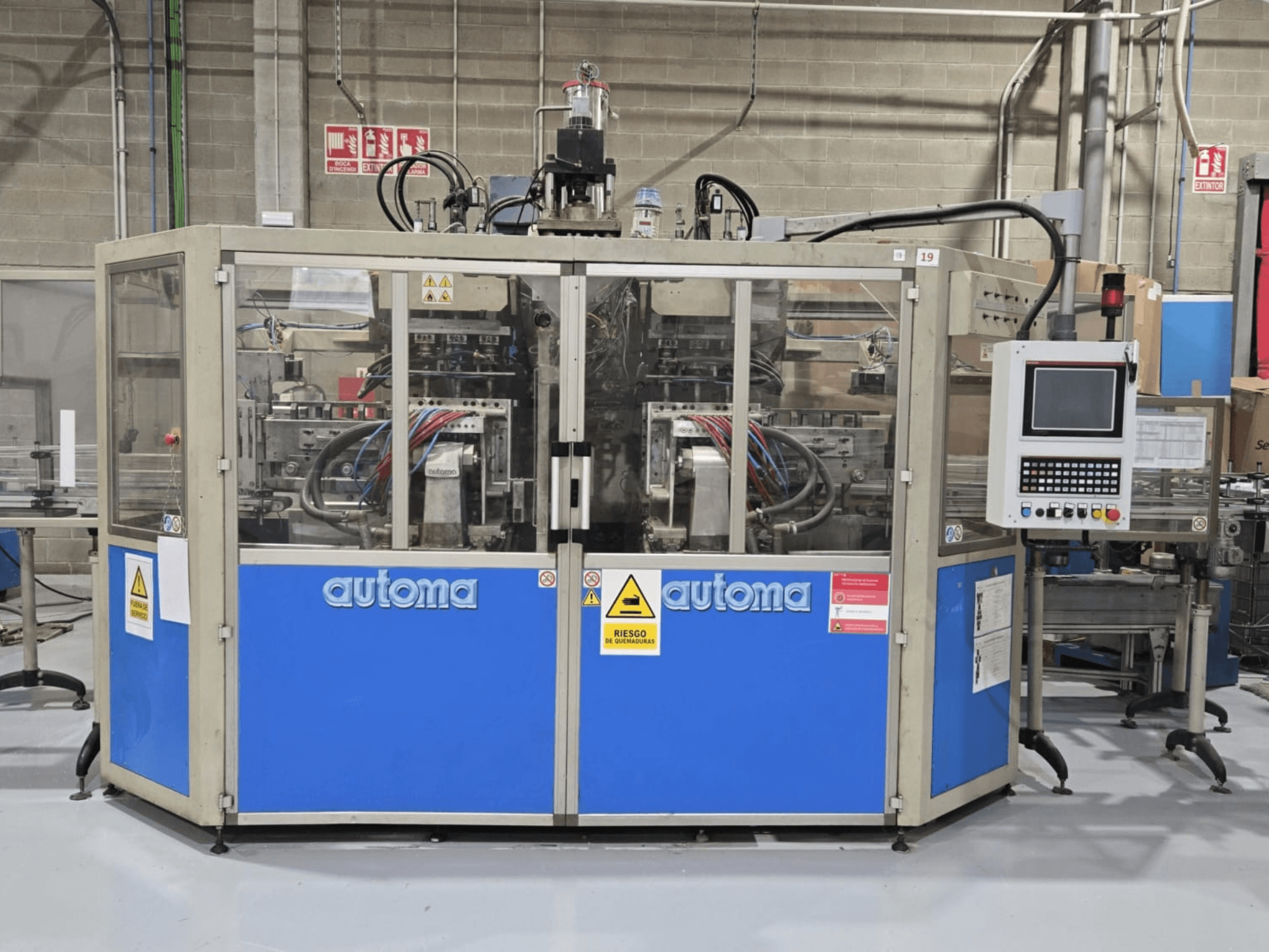 AUTOMA APEX AT500D blow moulding machine front view, featuring control panel and various hoses, set in a factory environment.