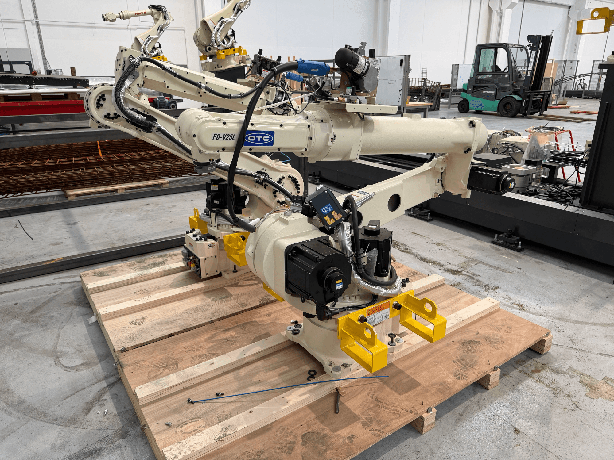 OTC Daihen FD19-V25L robot arm in front view, featuring yellow gripper claws and visible mechanical components on a wooden pallet.