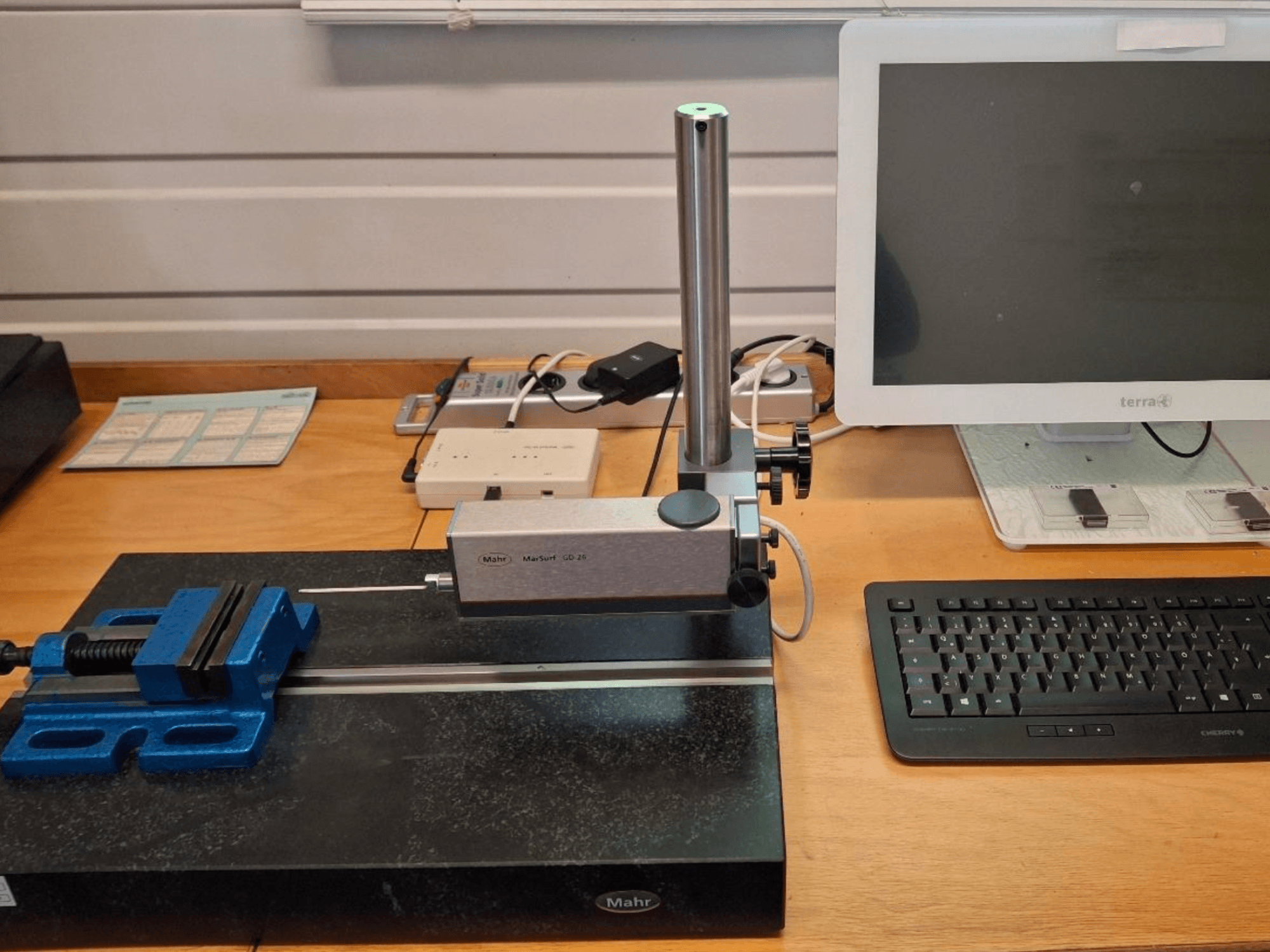 MAHR MARSURF GD 26 CMM on a workbench, featuring a measurement probe, a blue vice, and a computer monitor. Front view.