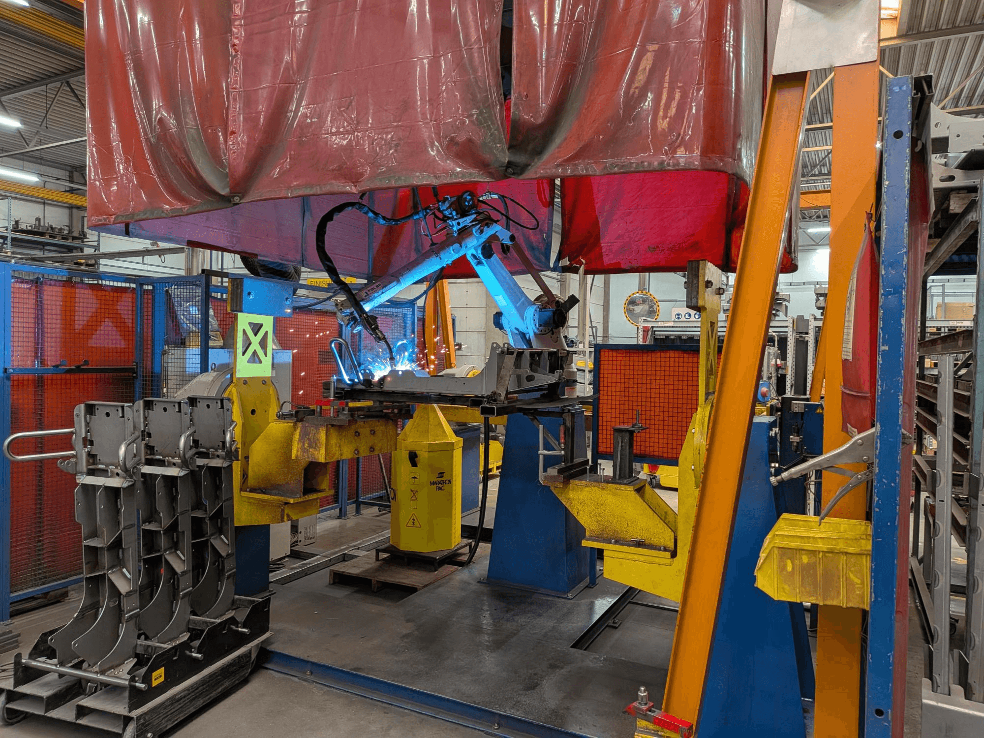 Welding robot OTC Daihen DR4200 in action, viewed from the front, featuring bright blue welding arc and protective cover.