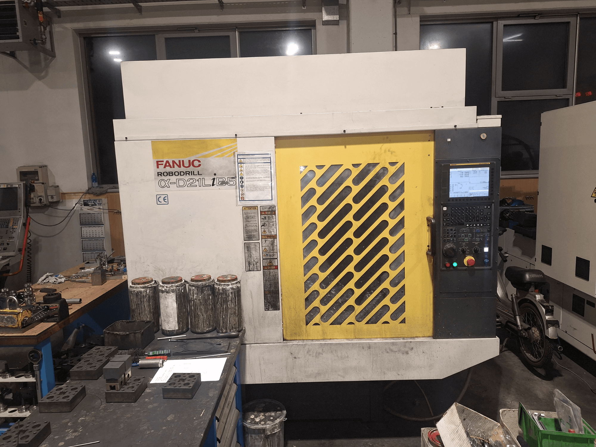 Front view of FANUC Robodrill α-D21LiB5, showing control panel, yellow grille, and nearby tools on a workbench.
