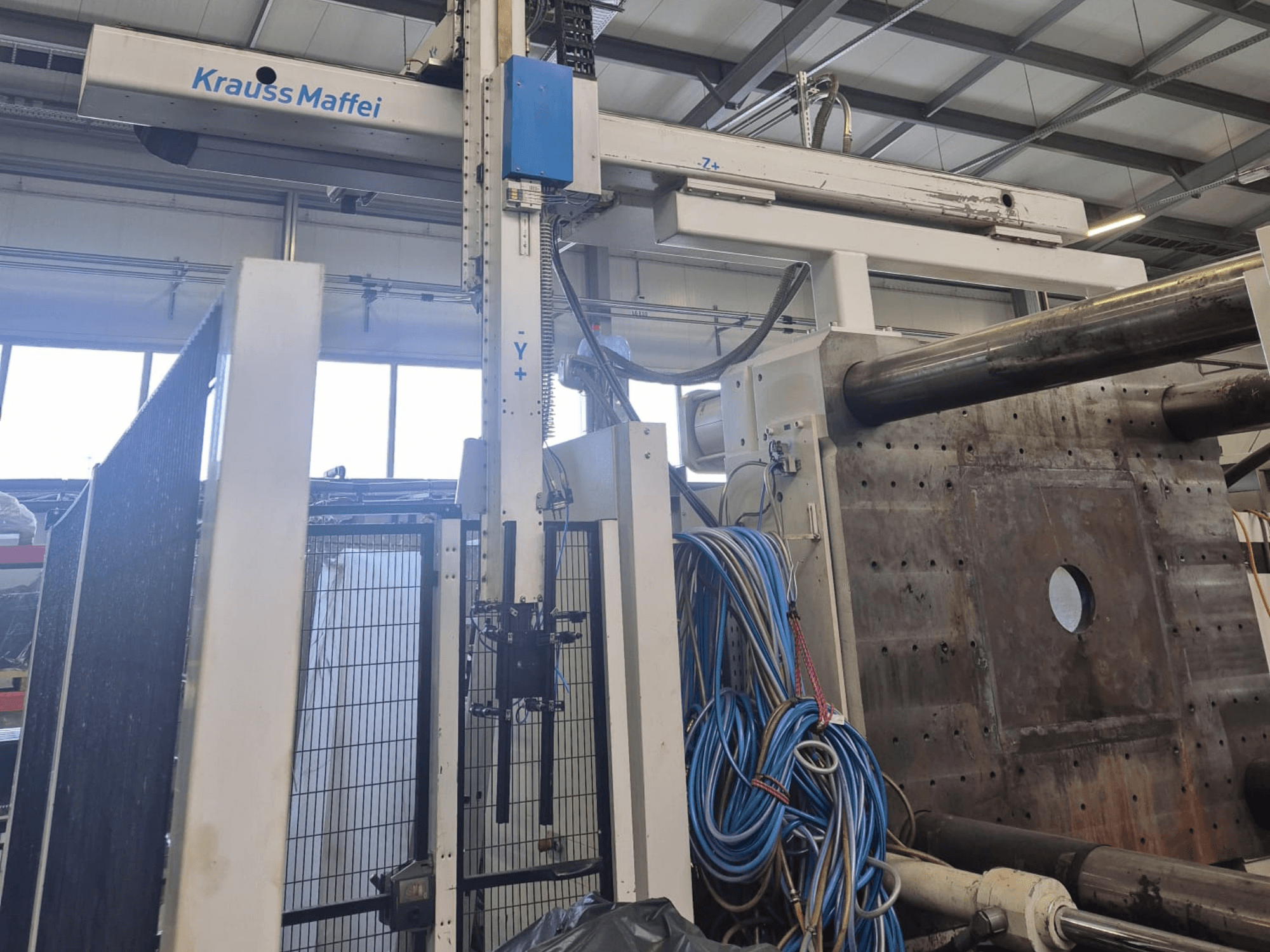 Krauss Maffei 1300-12000 MX hydraulic injection moulding machine, front view with mechanical arms and hydraulic connections.