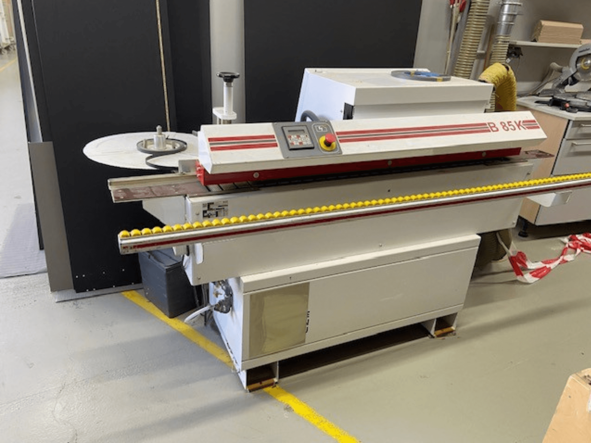 B 85K edge banding machine in white and red, front view, features a control panel and yellow roller for material feed.